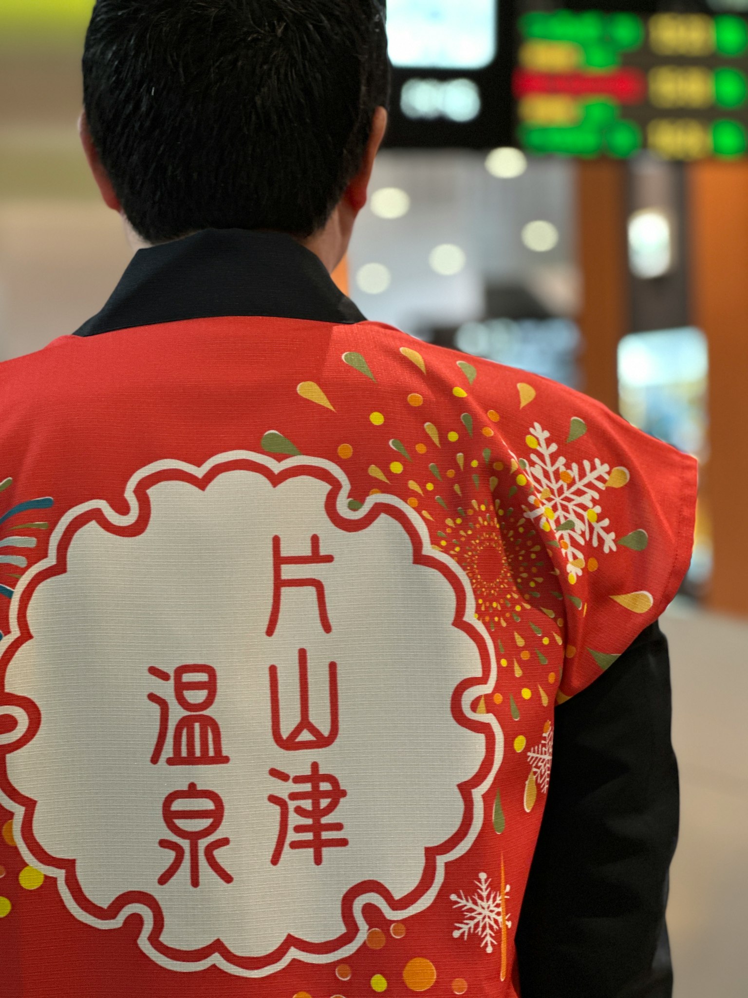 Persona che indossa una giacca rossa con caratteri kanji per Katayamazu Onsen sulla schiena
