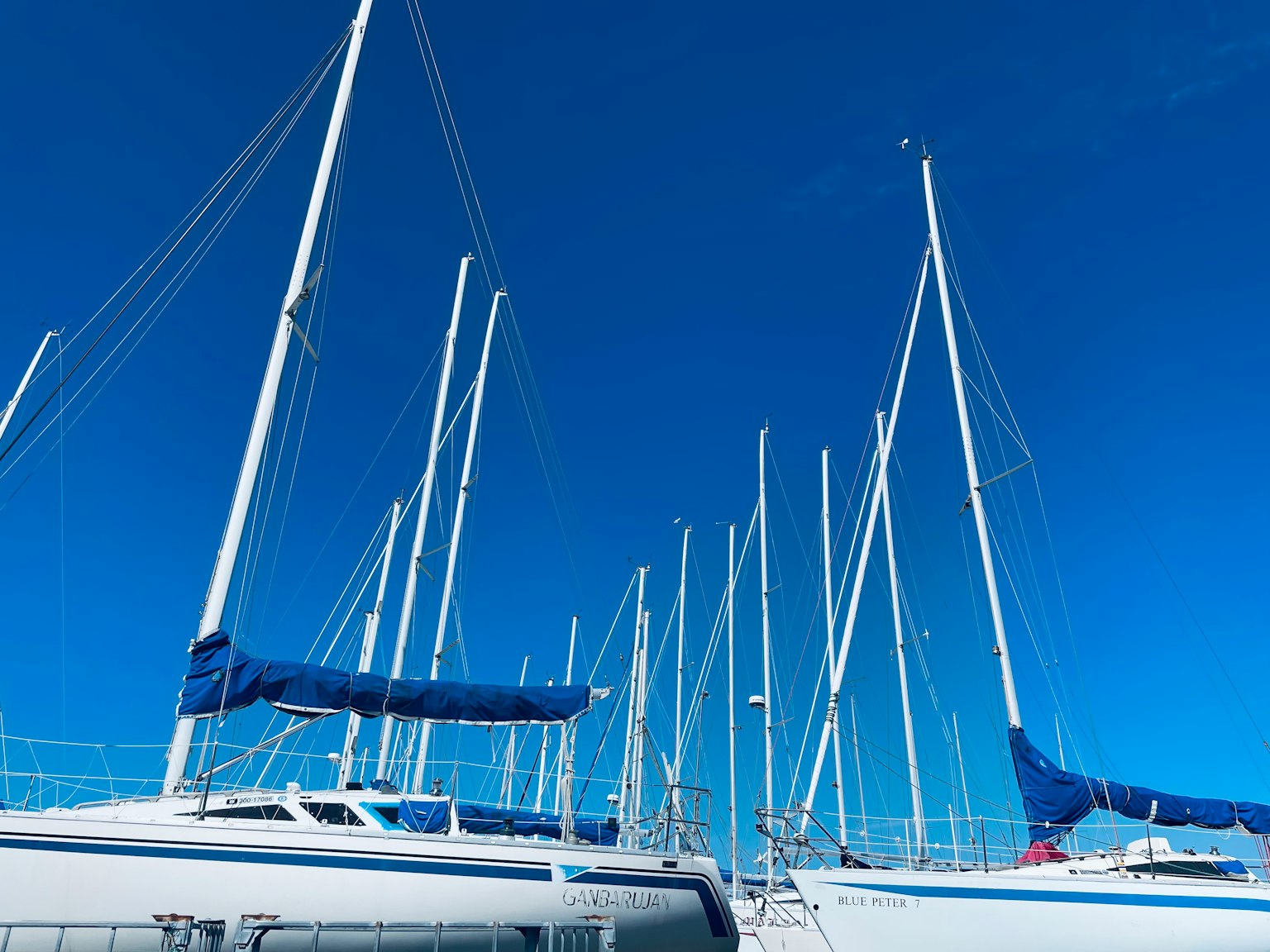 Mehrere Masten und Segel von Segelbooten vor einem blauen Himmel