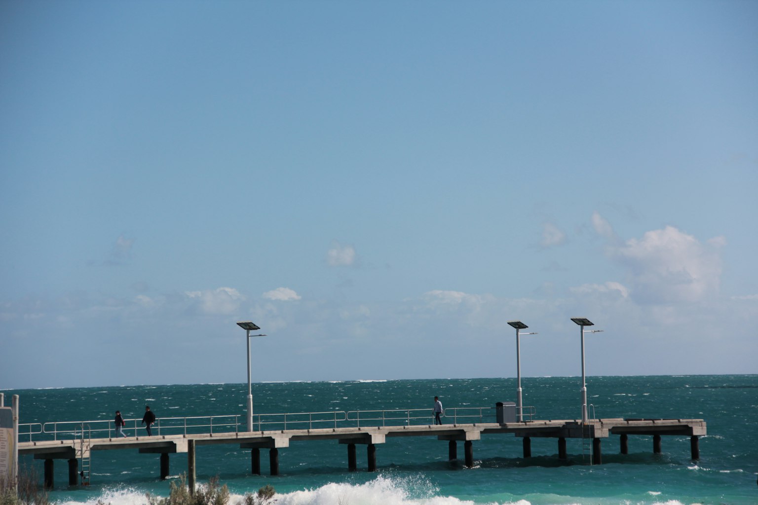 Steg, der ins blaue Meer mit brechenden Wellen führt