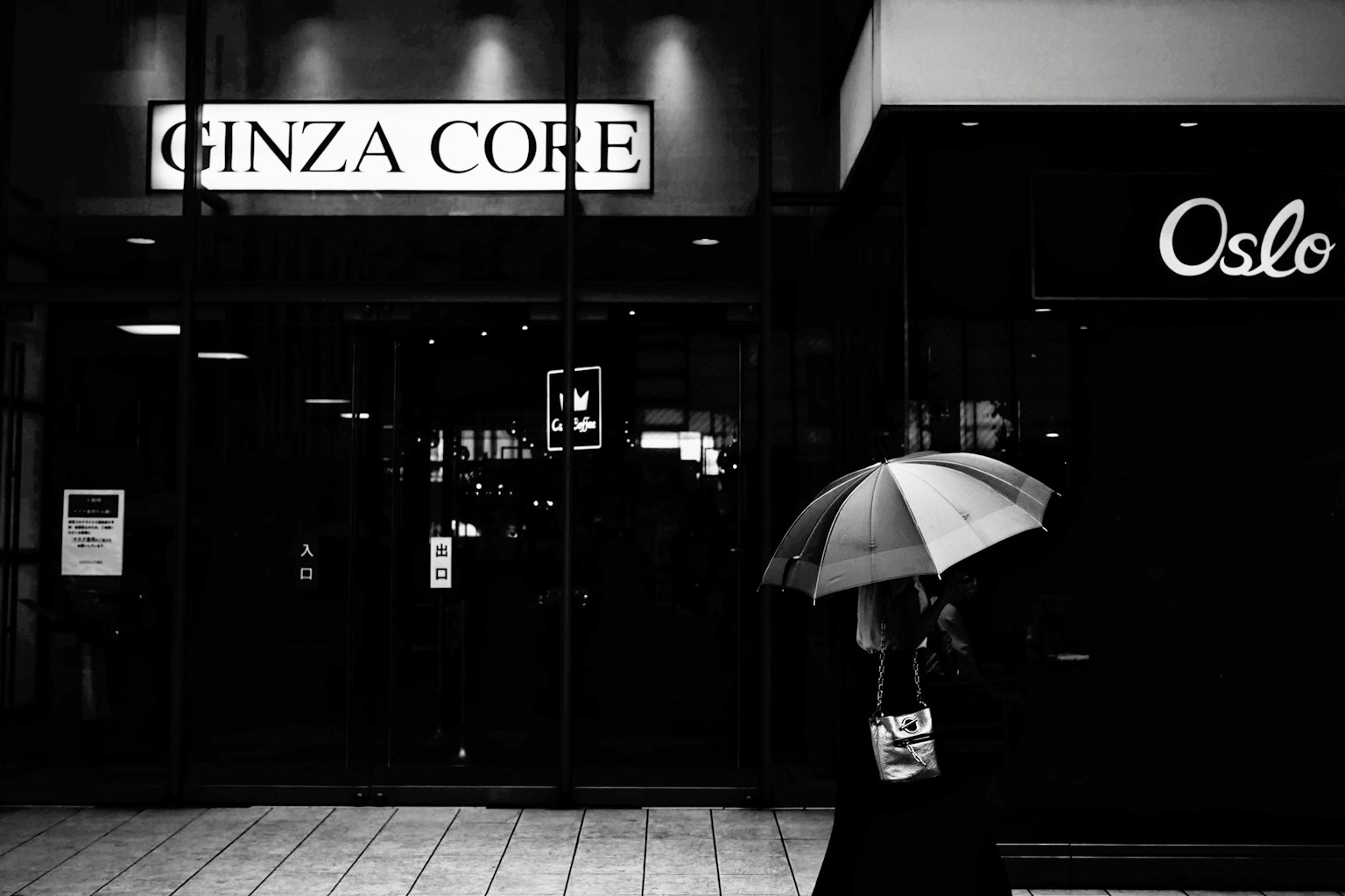 Black and white photo of a woman holding an umbrella in front of Ginza Core