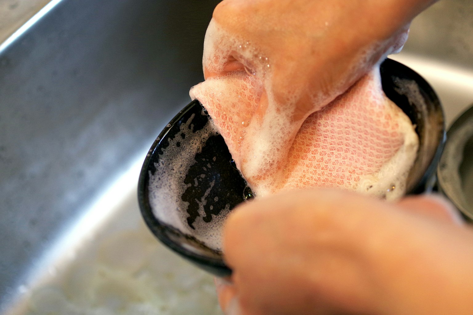 Tangan mencuci piring dengan spons berbusa