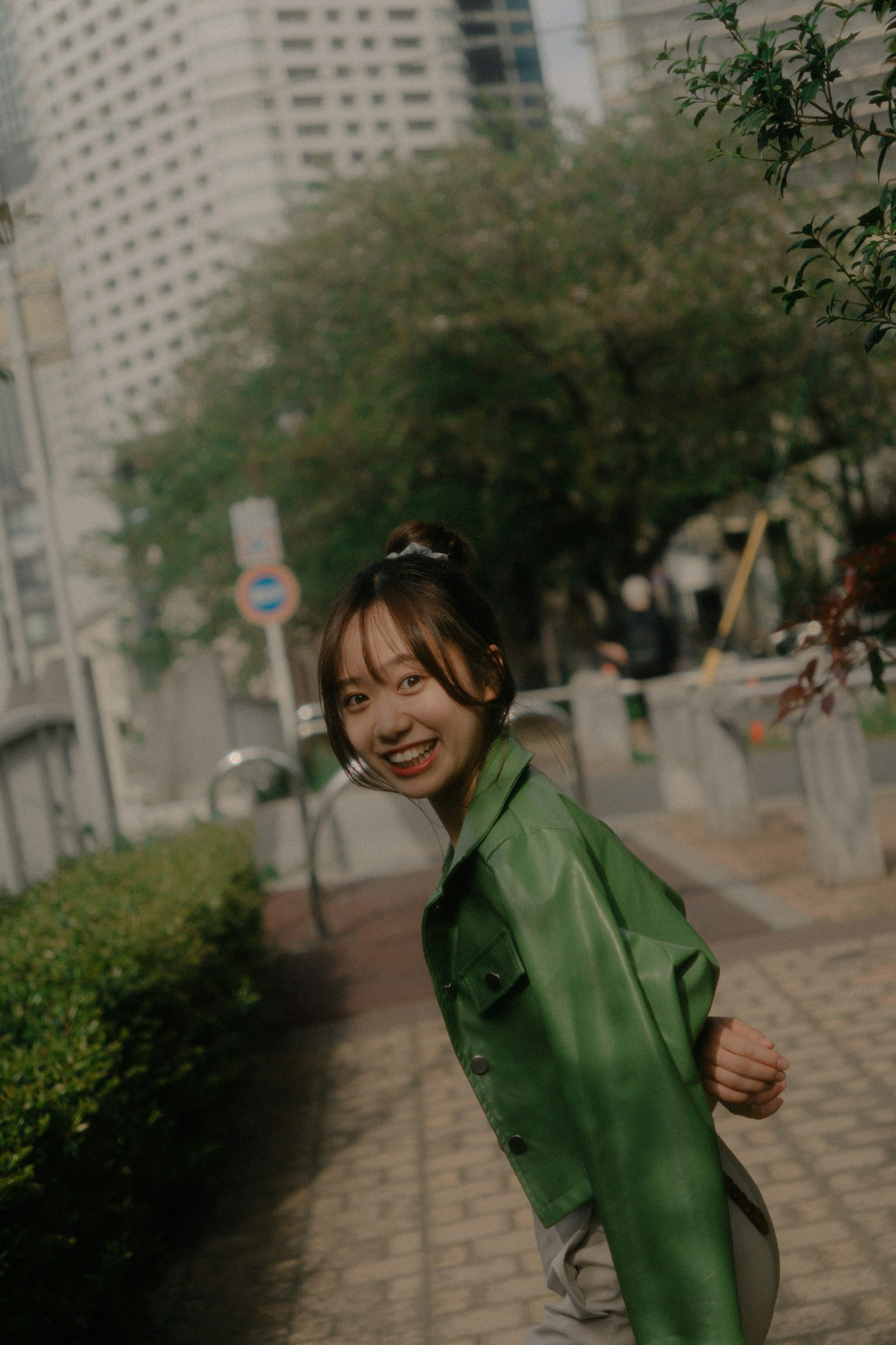 Una donna con giacca verde che sorride mentre cammina in un ambiente urbano