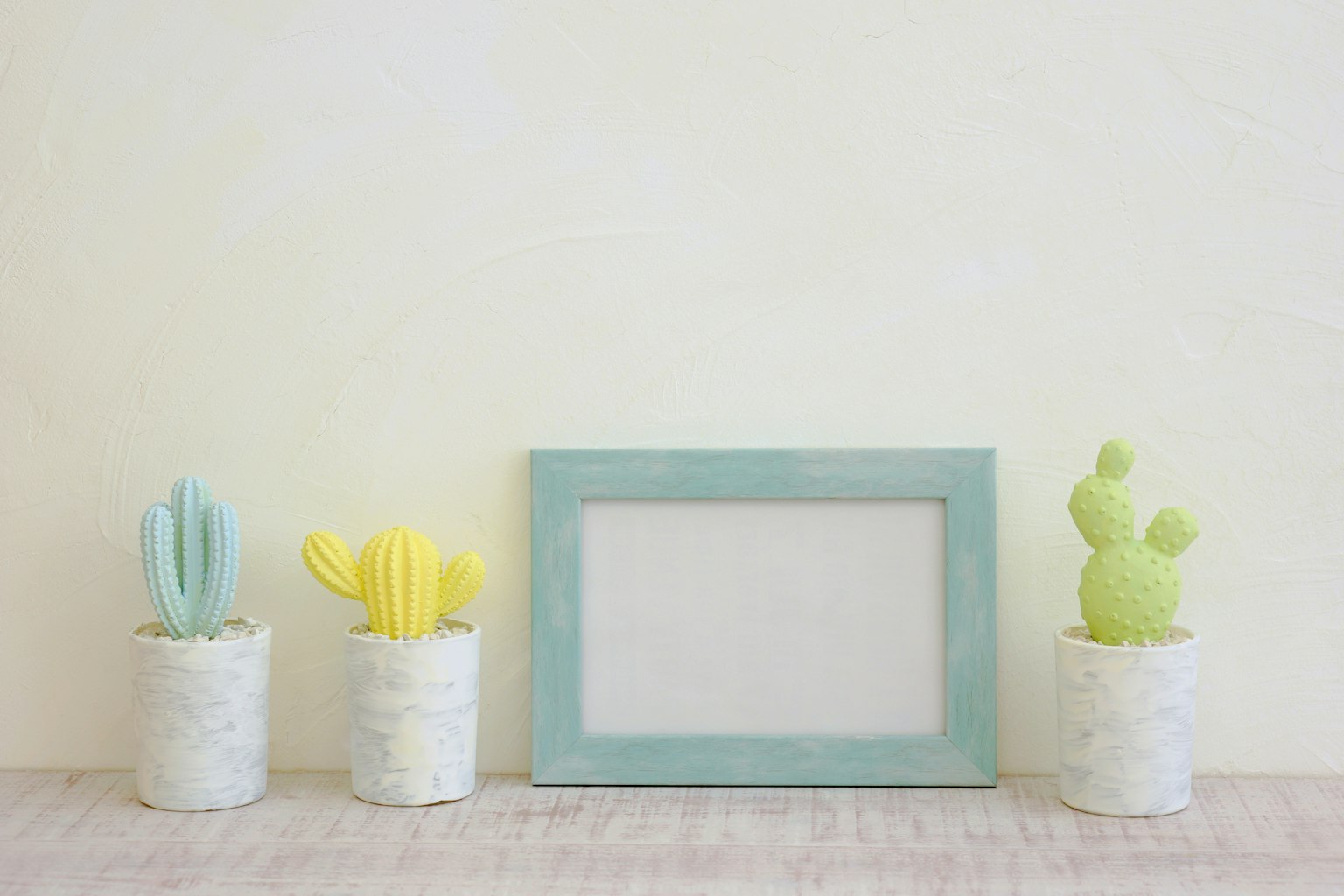 Vasi di cactus colorati e una cornice vuota disposti su un muro chiaro