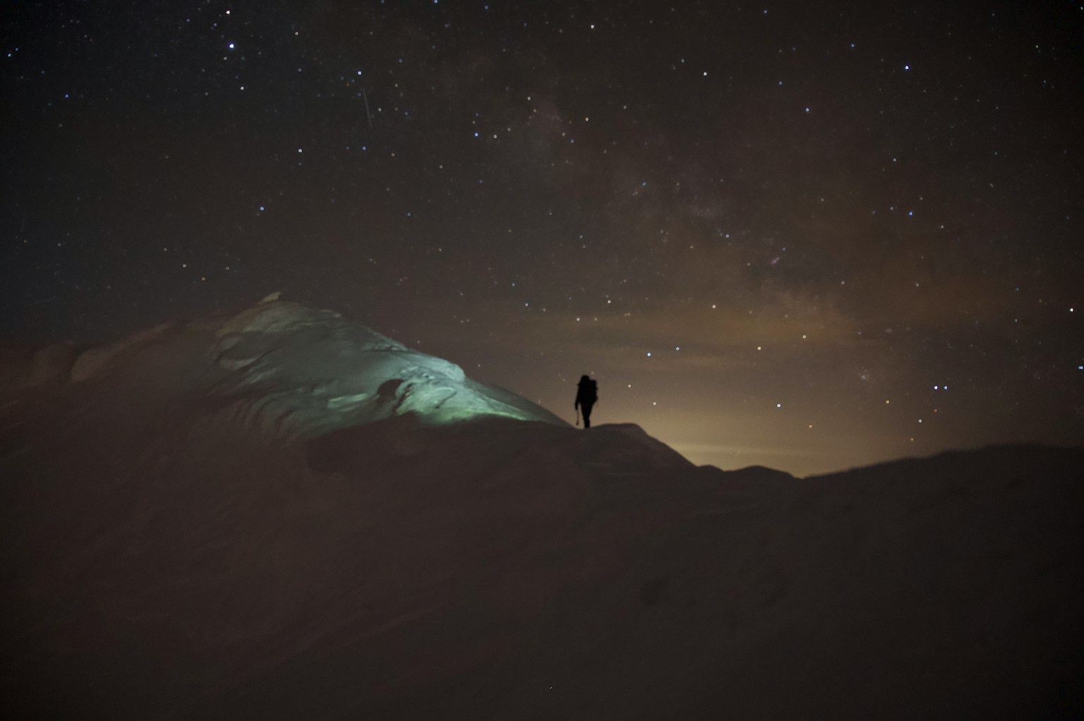 Silhouette einer Person, die auf einem dunklen Berggipfel unter einem sternenklaren Nachthimmel steht