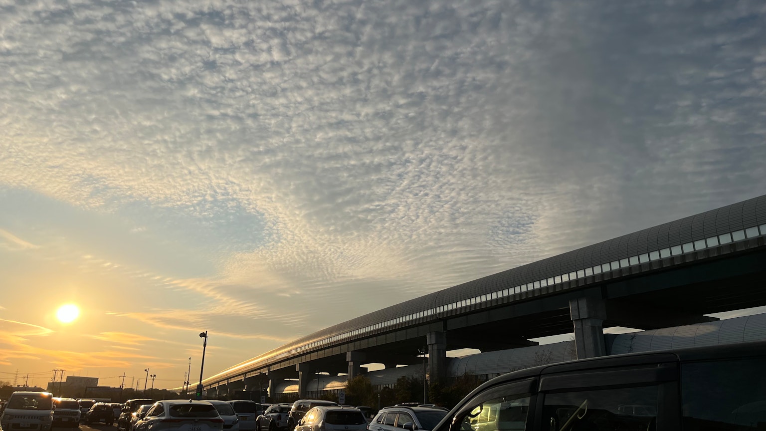Vista panoramica di nuvole ondulate nel cielo al tramonto sopra le auto parcheggiate sotto un viadotto