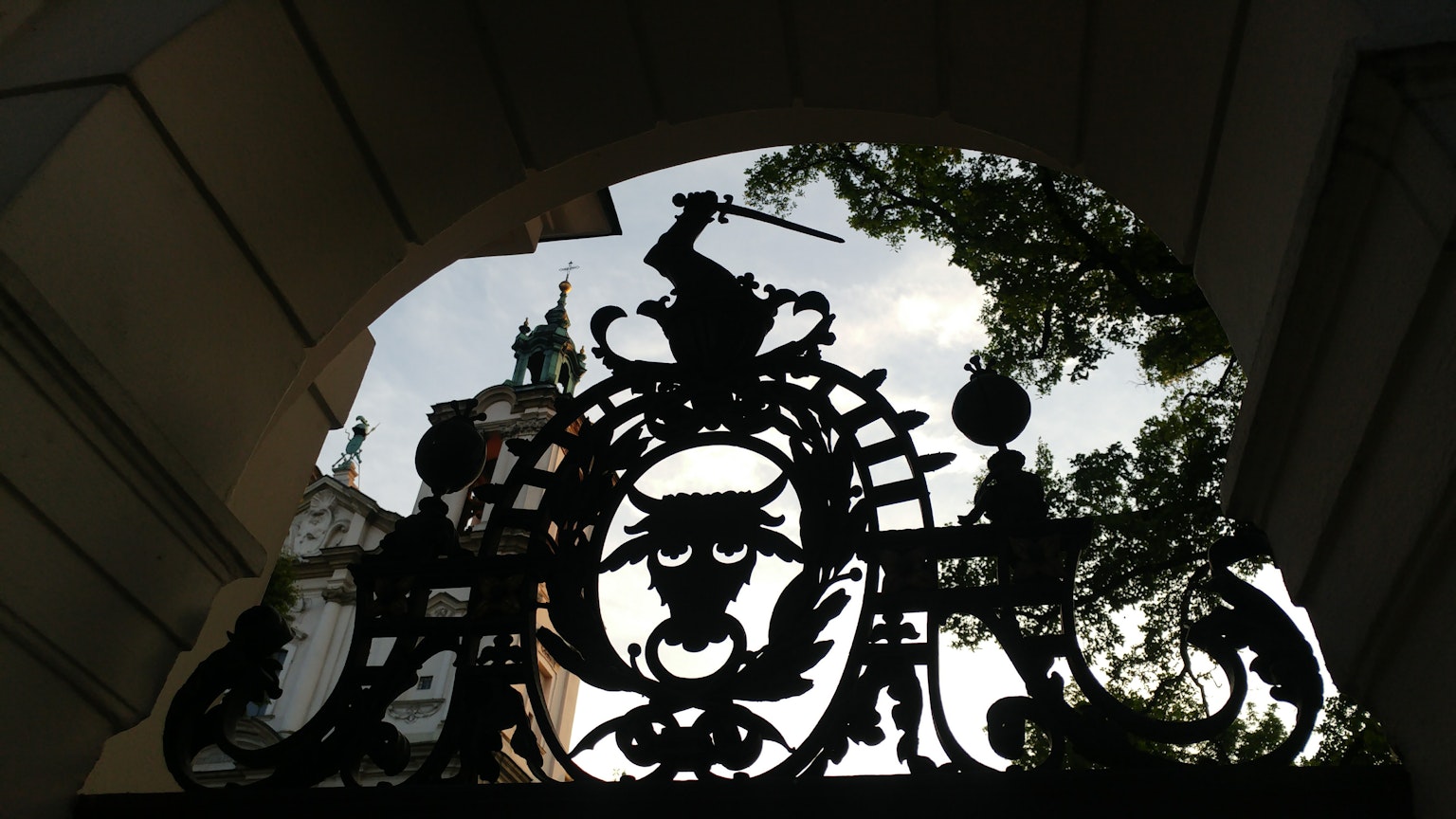 Silhouette of an ornate wrought iron gate with trees and sky in the background