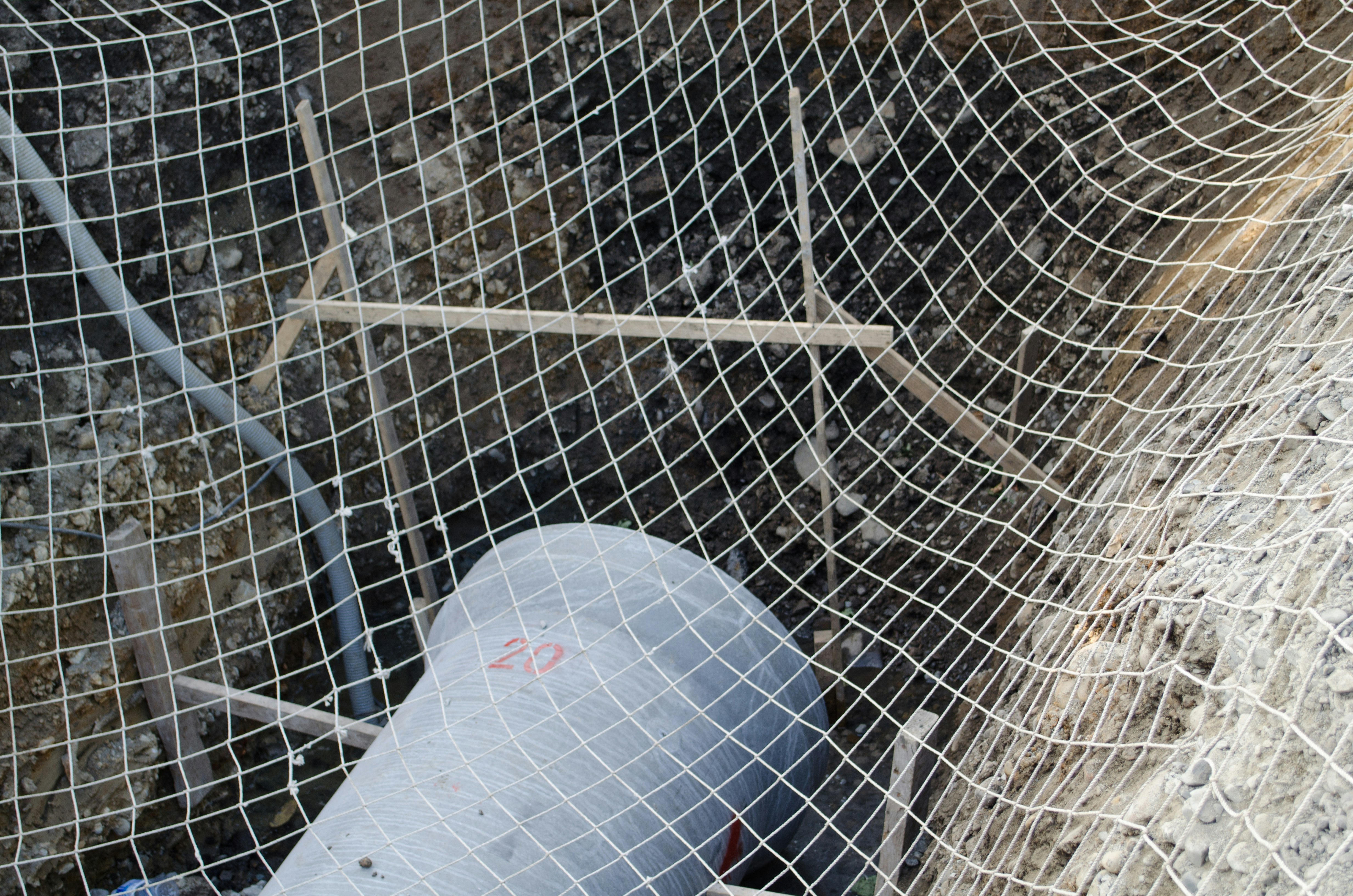Part of a construction site with netting visible along with metal pipes and concrete