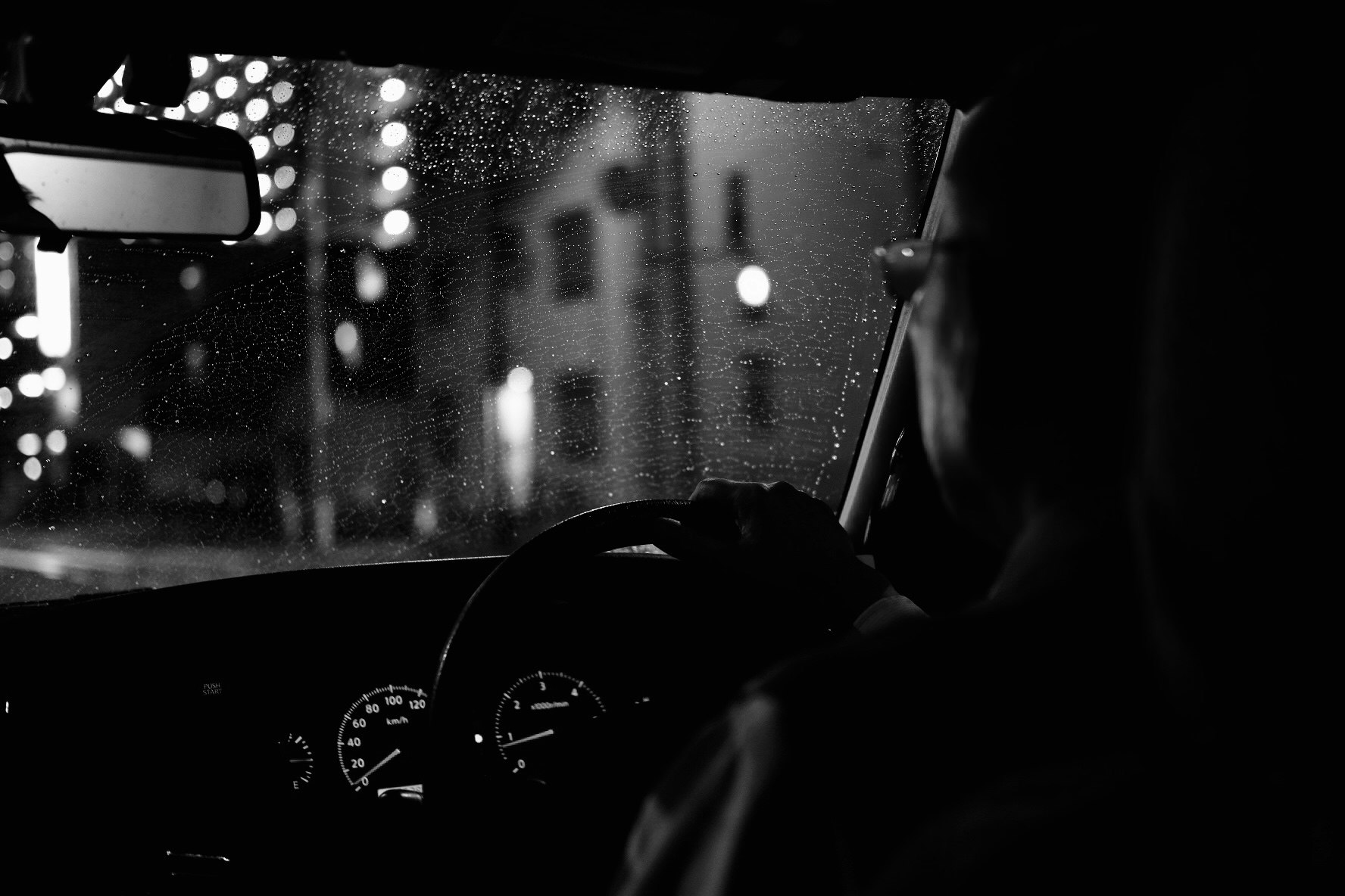 雨粒のついた窓越しに運転席の計器が光る夜の車内