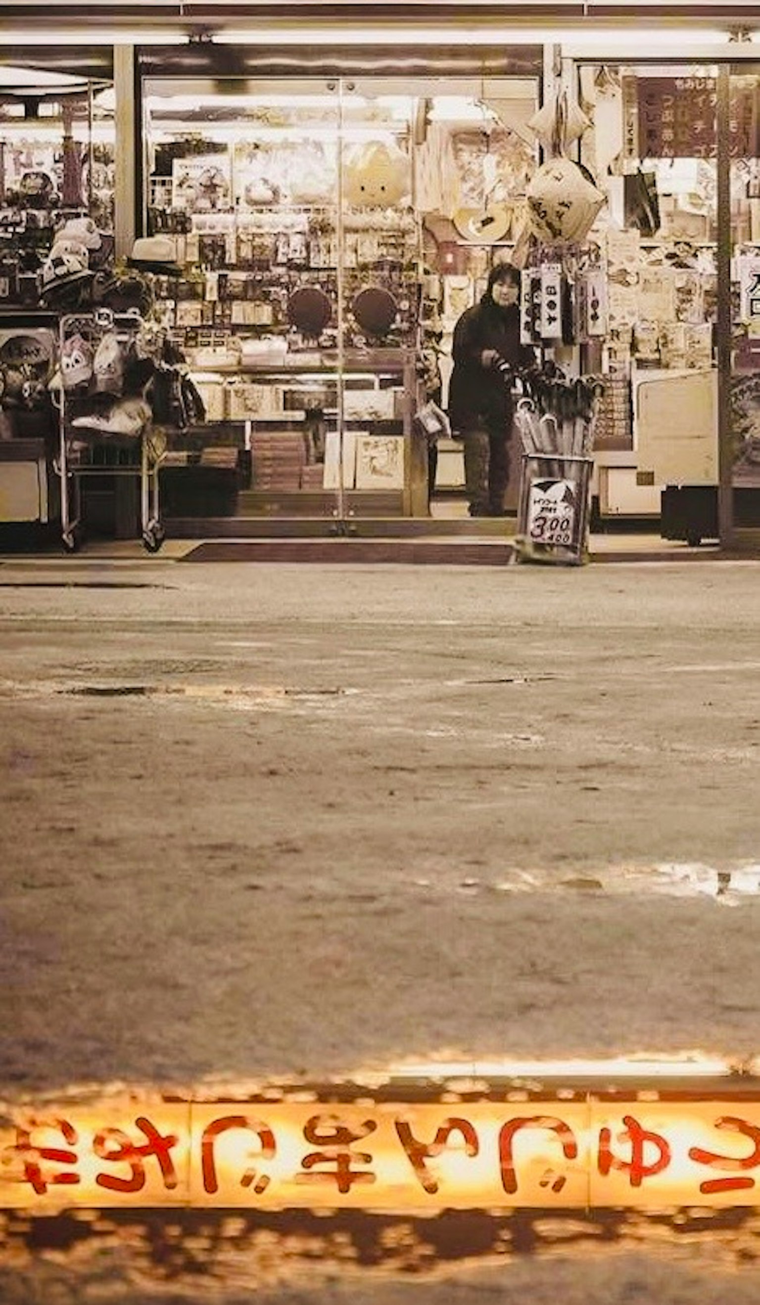 商店の前に立つ人と店内の様子が見える夜の街の風景