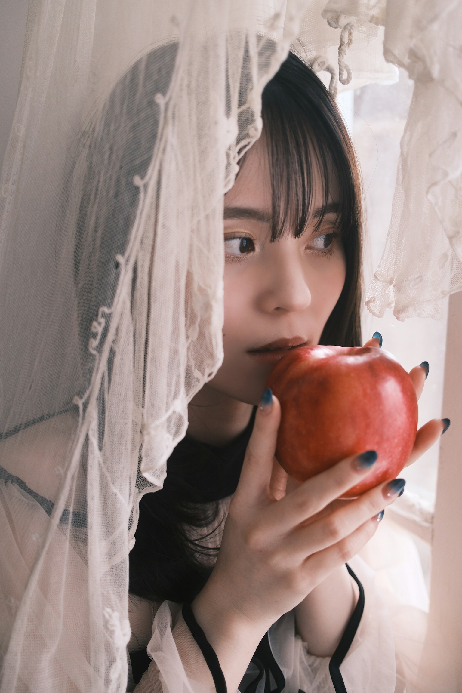 白いレースのカーテンの後ろにいる女性が赤いザクロを持っている