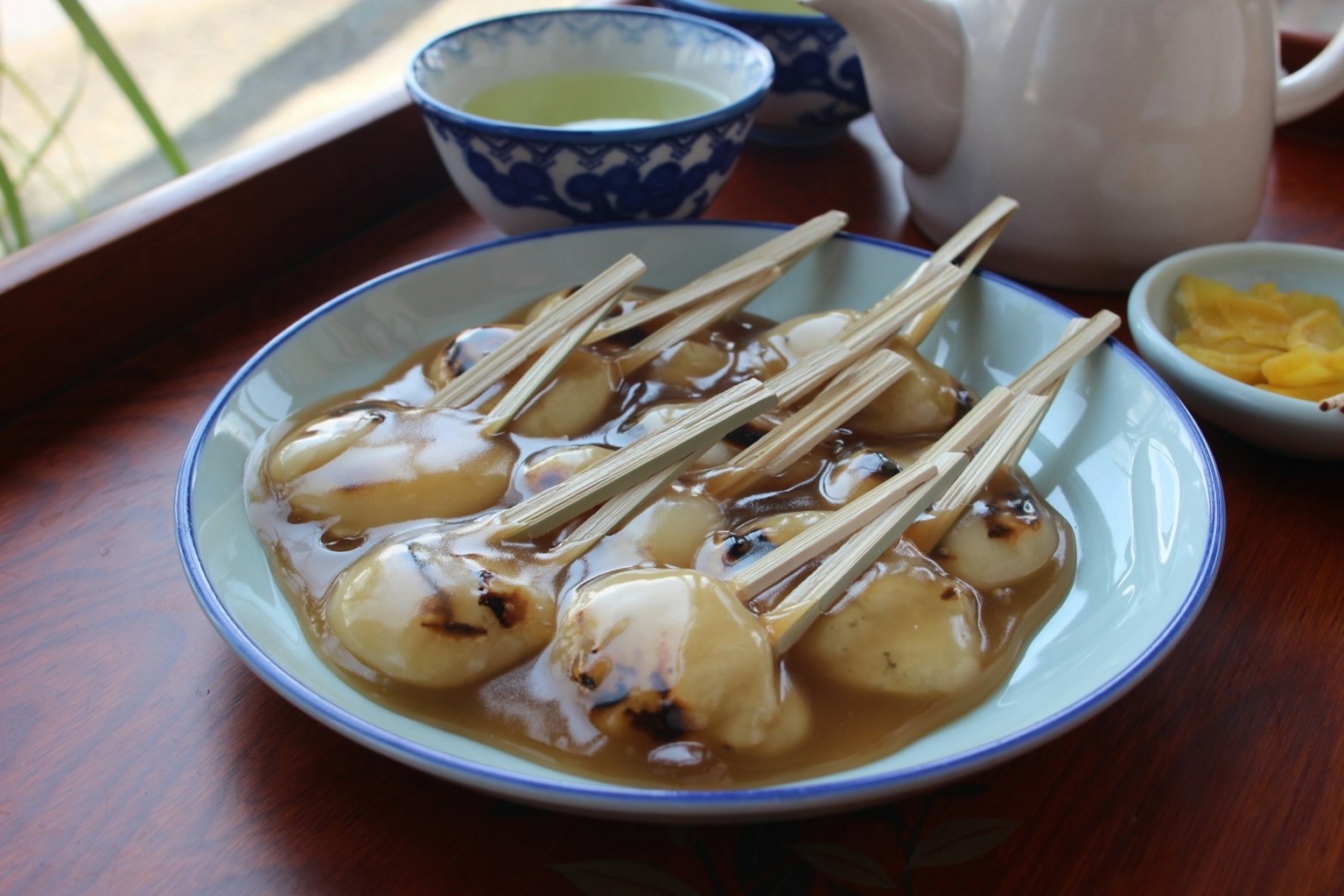 A plate of grilled rice dumplings on skewers with a cup of green tea