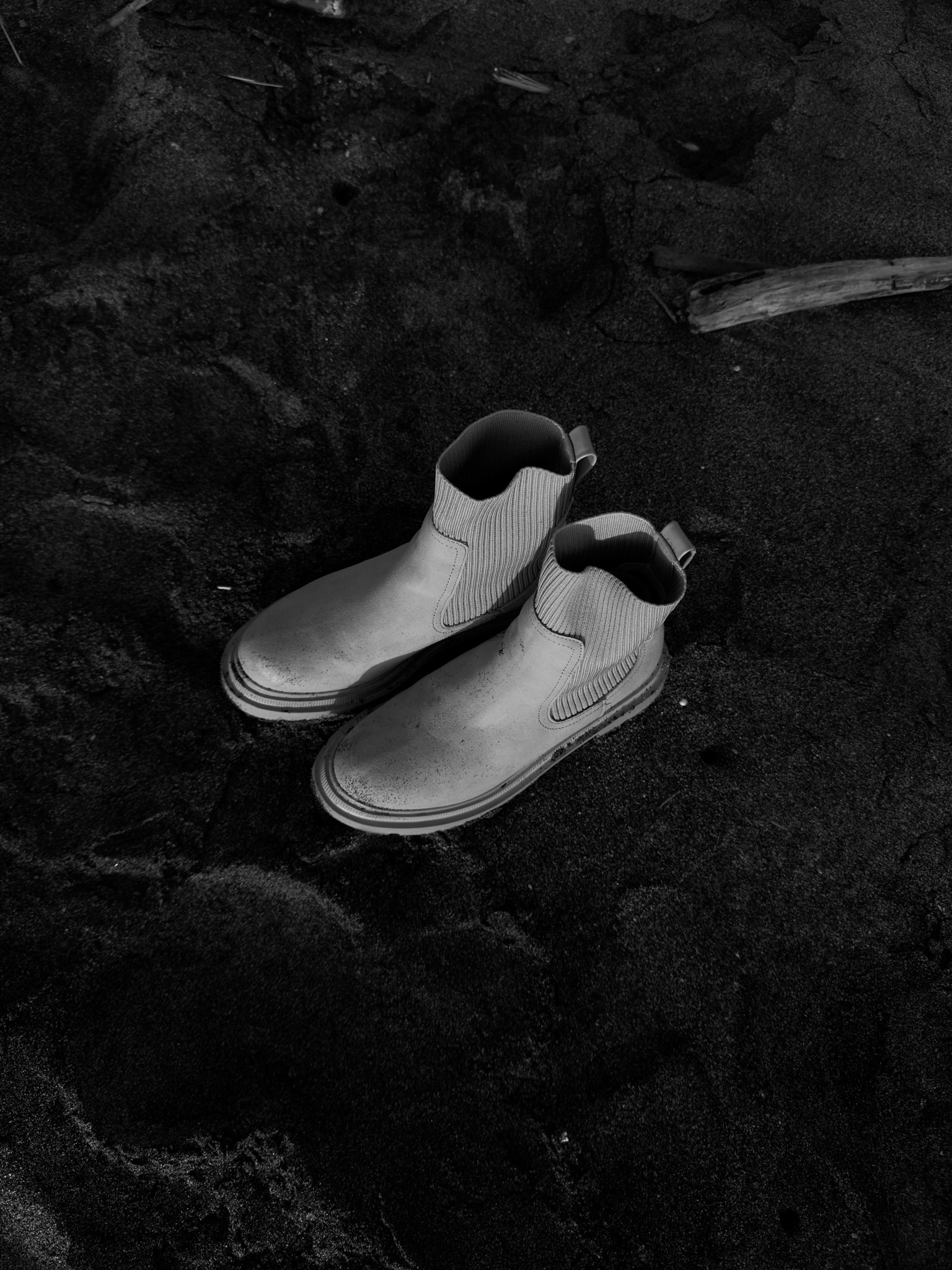 Sepatu putih diletakkan di atas pasir hitam