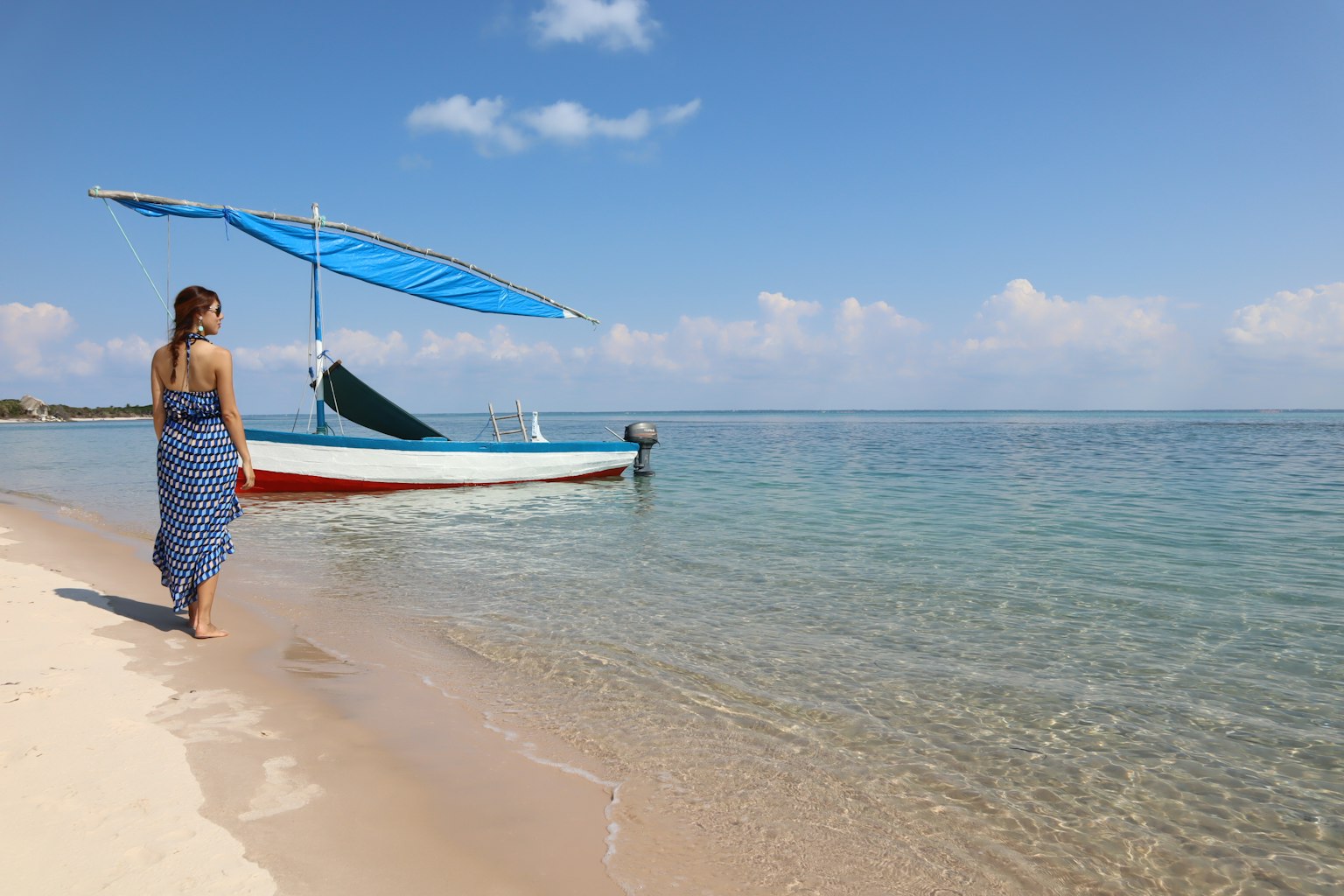 Femme marchant sur la plage vers un bateau avec un auvent bleu eau claire et ciel bleu