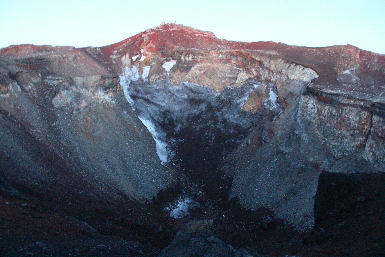 View of a volcanic crater featuring red rocks and gray soil