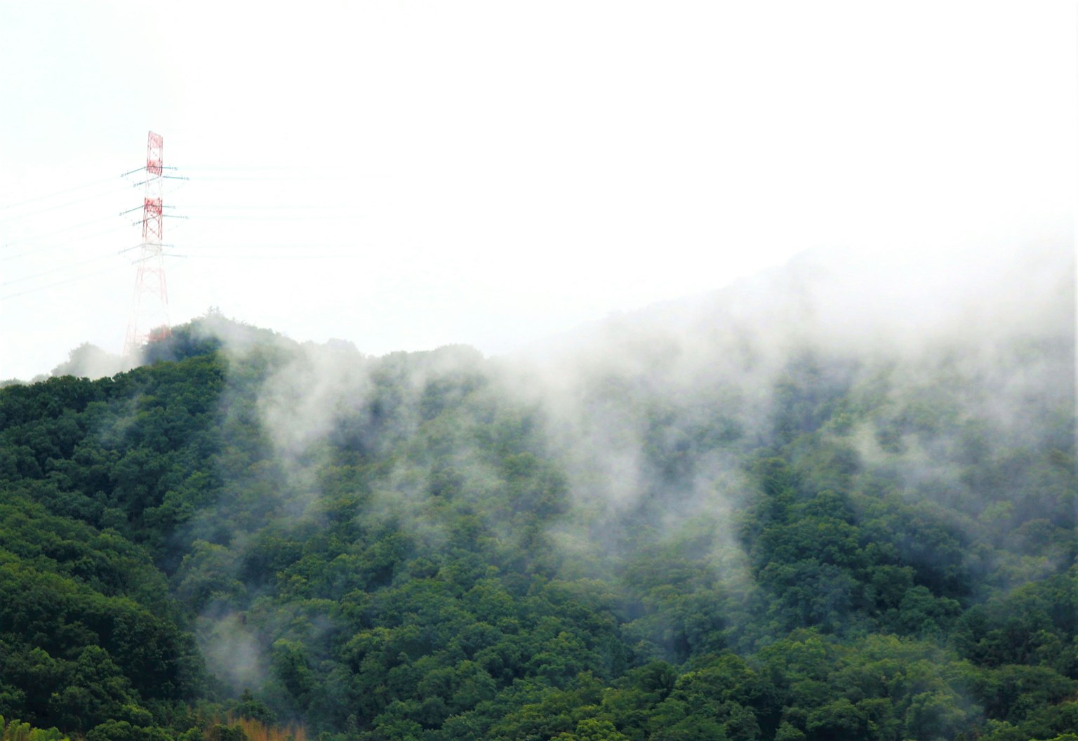 Pemandangan pegunungan yang diselimuti kabut dengan menara transmisi