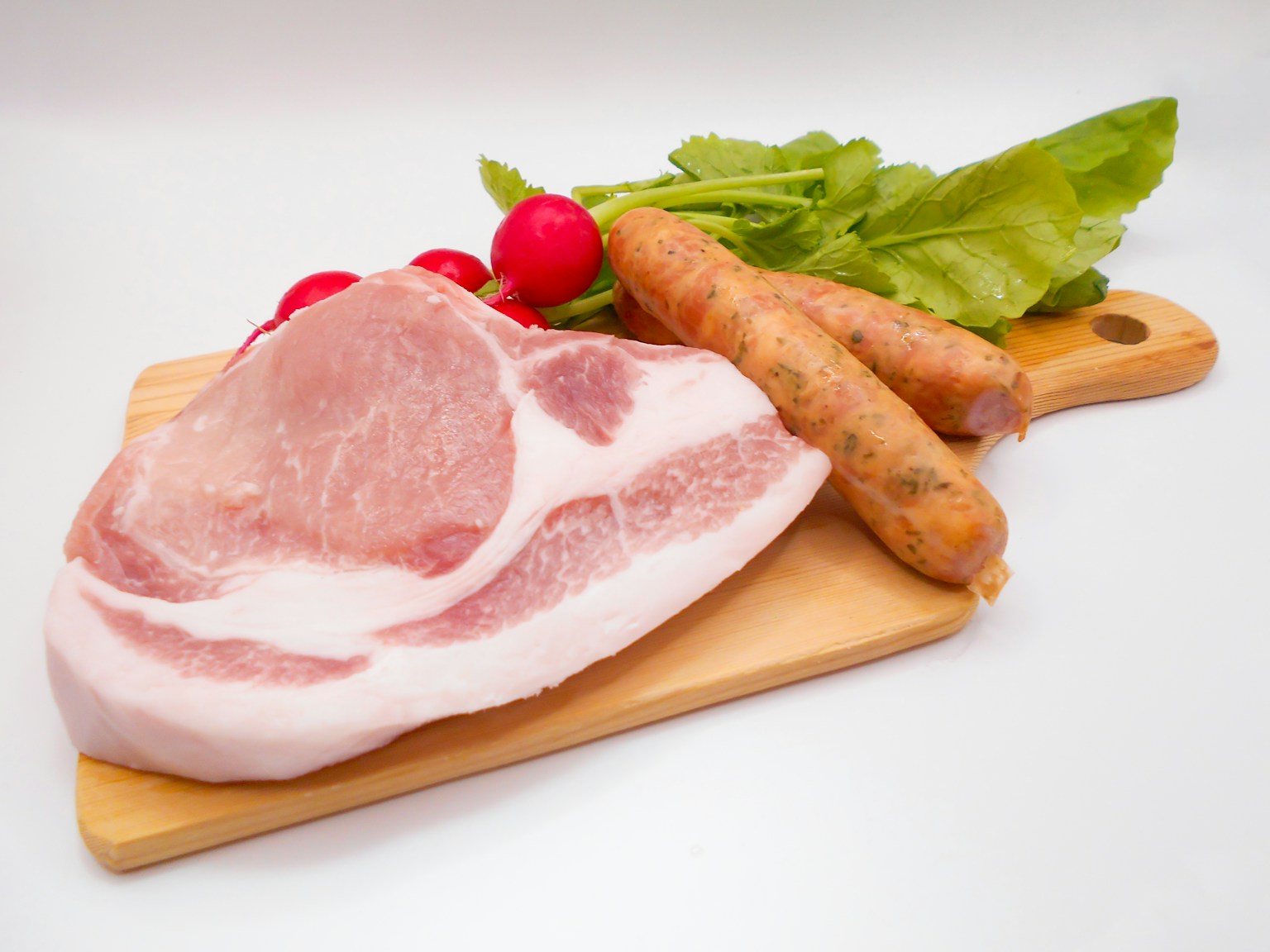 Sliced pork, sausages, radishes, and mint leaves arranged on a wooden cutting board