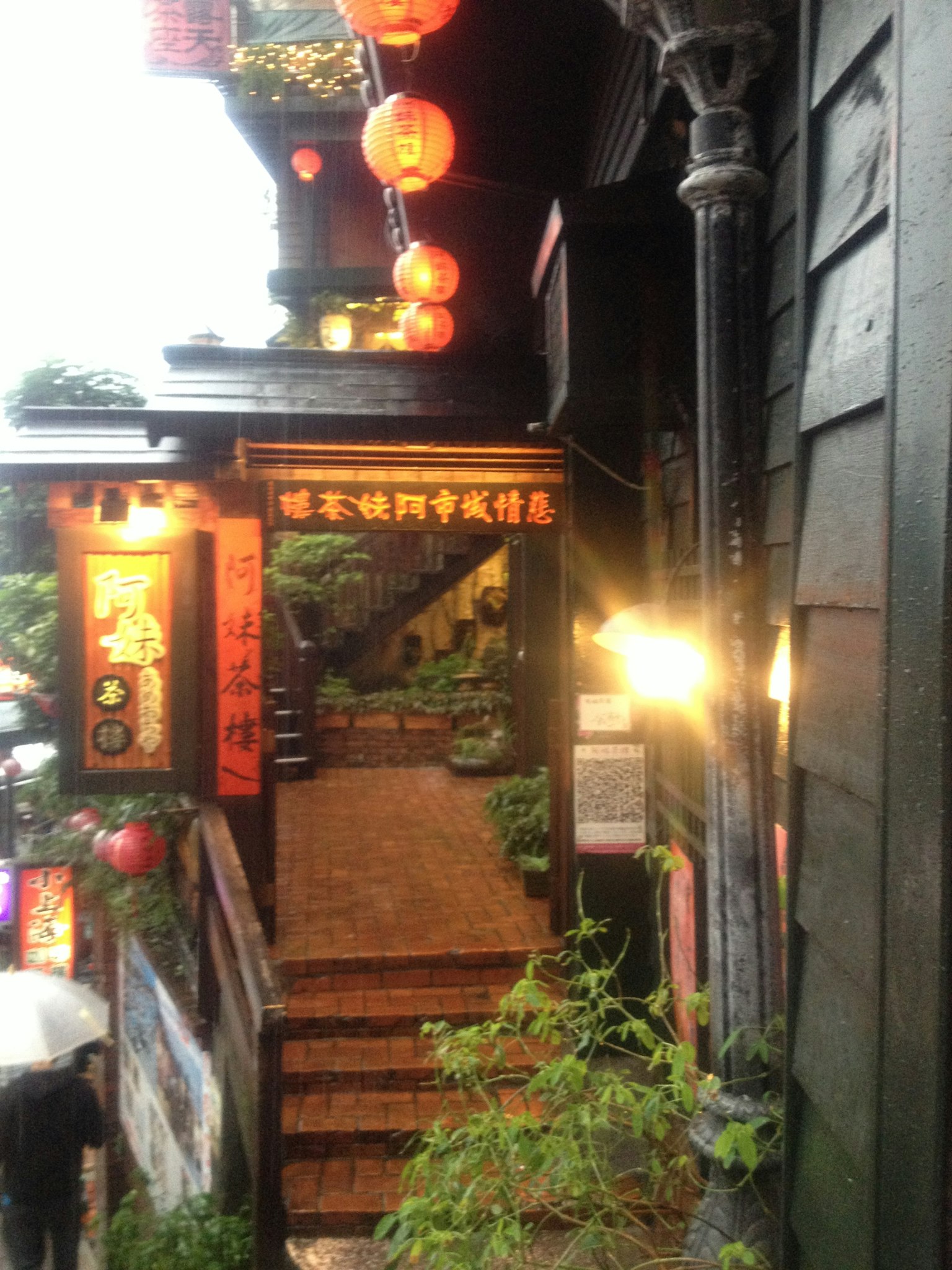 ทางเข้าของอาคารเก่าที่มีโคมไฟแขวนและพืชพรรณเขียวชอุ่มตามบันได