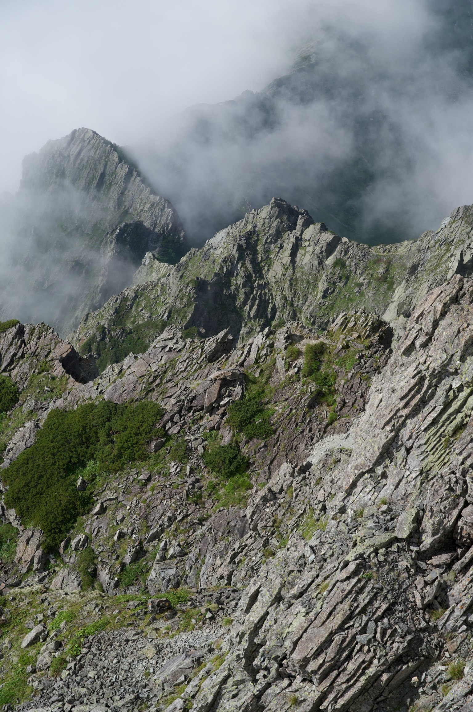 Cumbres montañosas rocosas cubiertas de nubes con manchas verdes