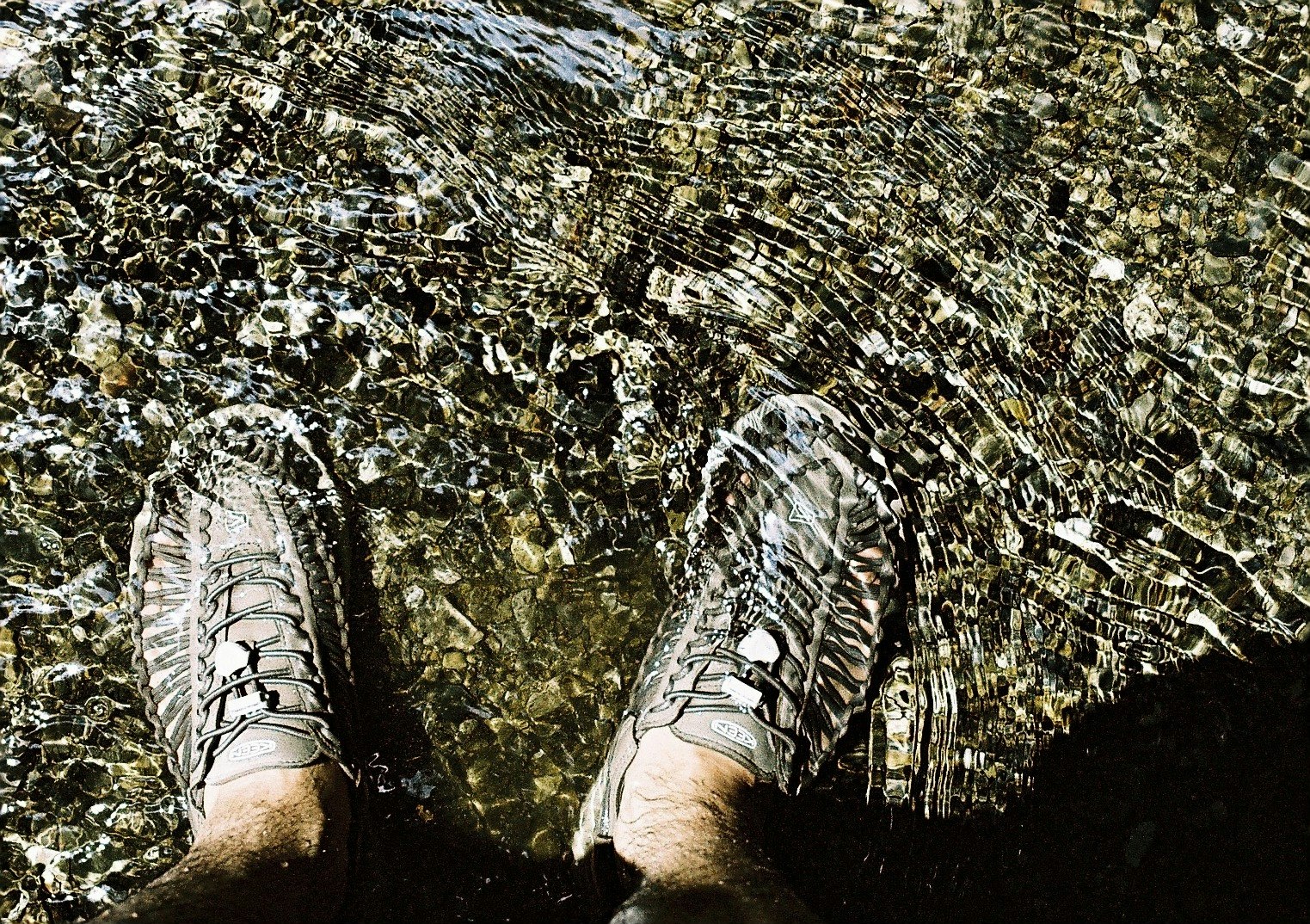 scarpe e piedi su rocce lungo la riva di un fiume