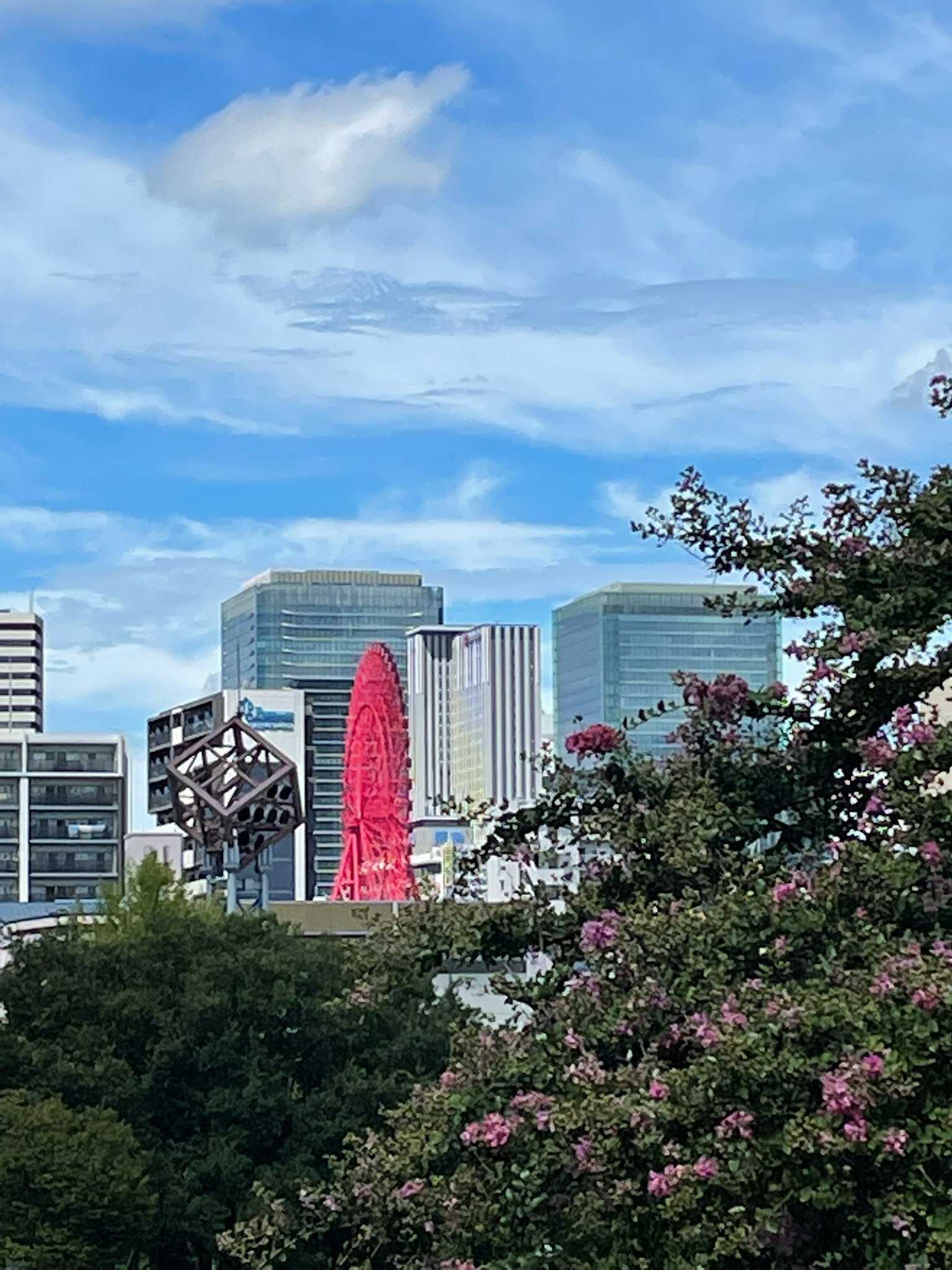 青空の下に高層ビルとピンクの花が見える都市の風景