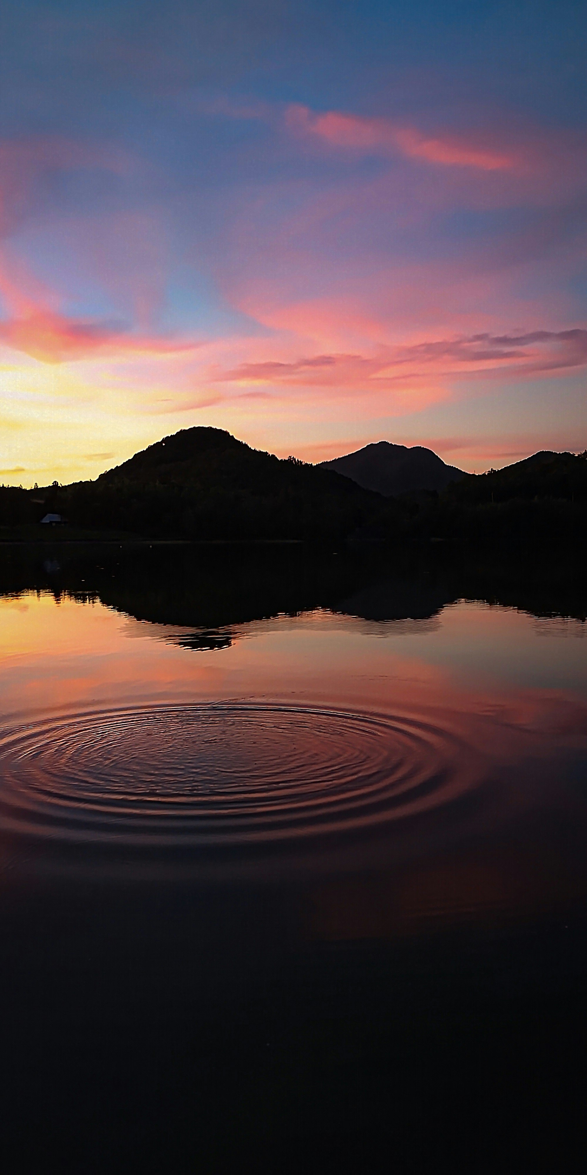 夕焼けに染まる湖面の波紋と山並み