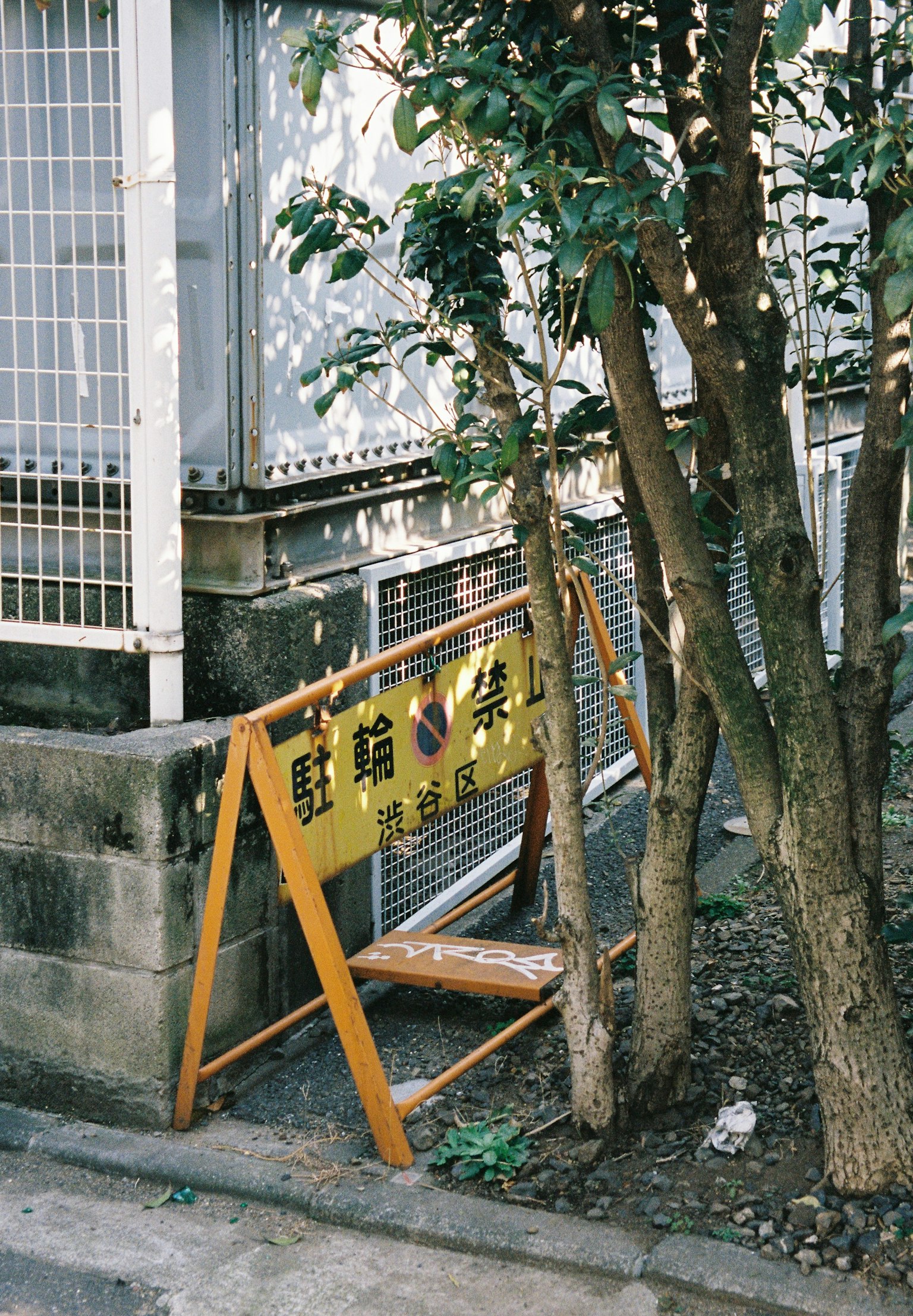 Narrow street scene with a yellow sign and green trees