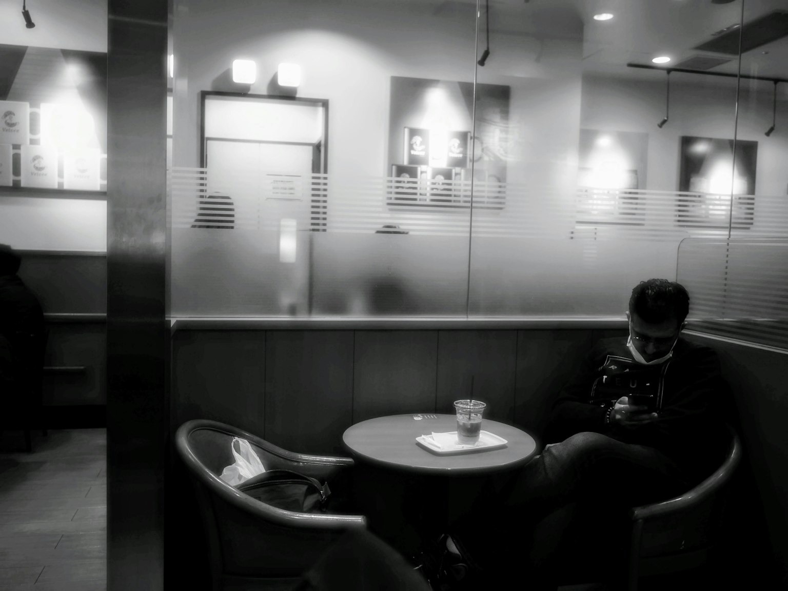 Seorang pria berpakaian hitam duduk di kafe sepi dengan kopi di atas meja