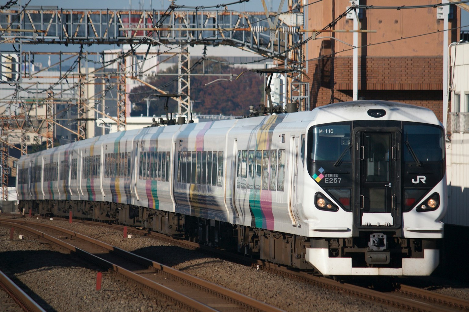 รถไฟสีขาววิ่งบนรางกับท้องฟ้าสีฟ้าใสและอาคารในพื้นหลัง