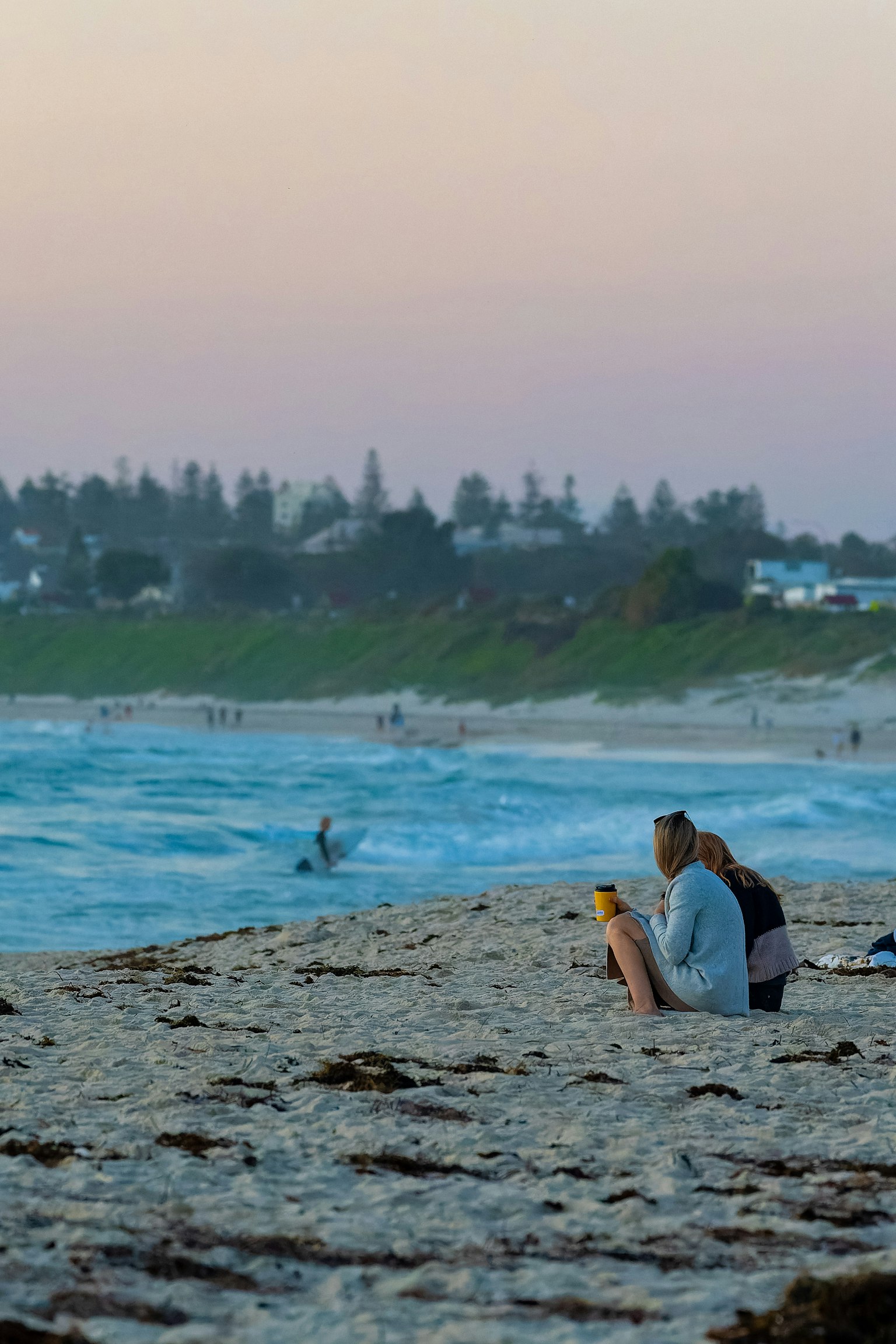 Pasangan duduk di pantai dengan ombak di latar belakang