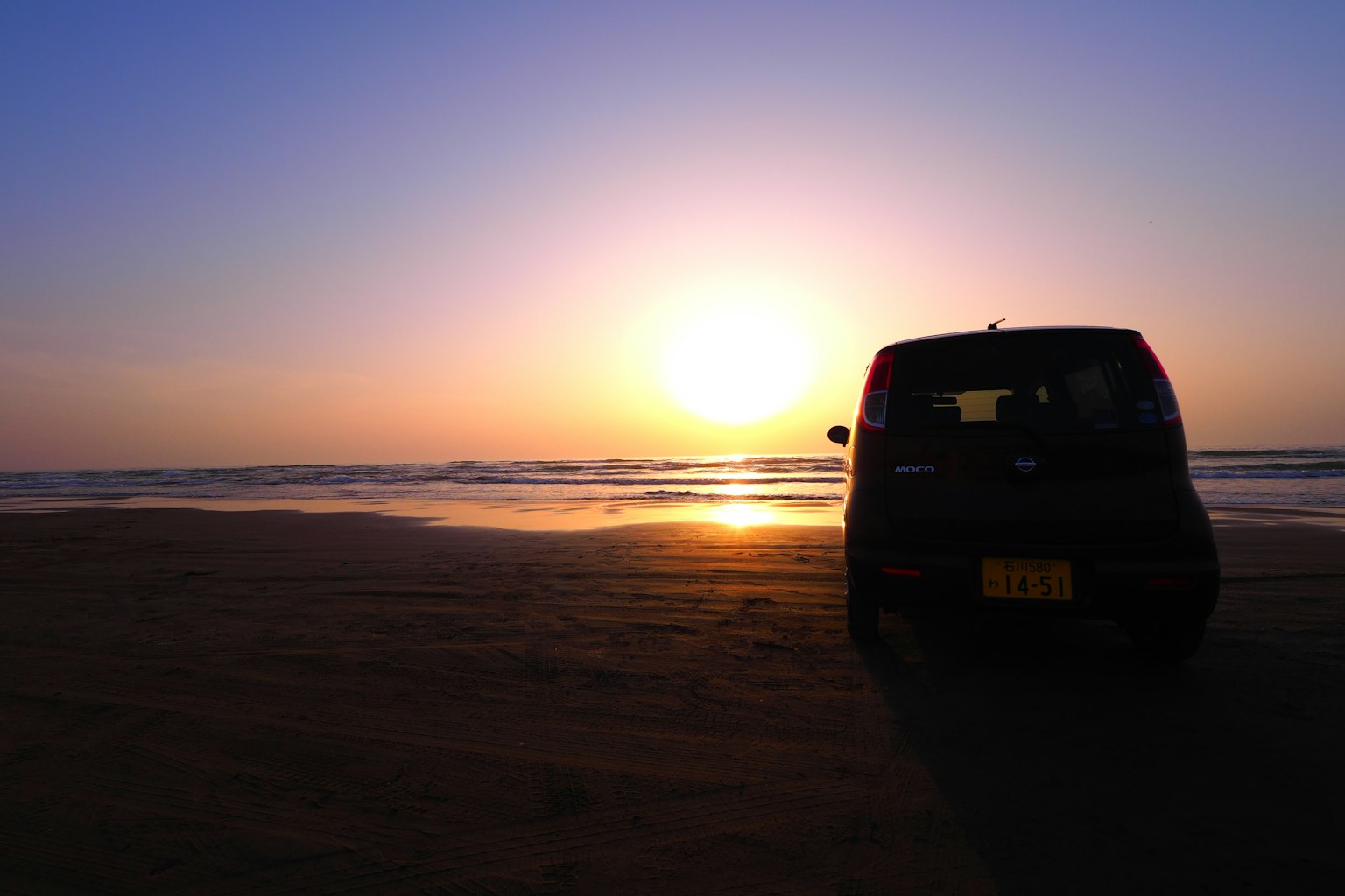 Coche negro estacionado en la playa con atardecer