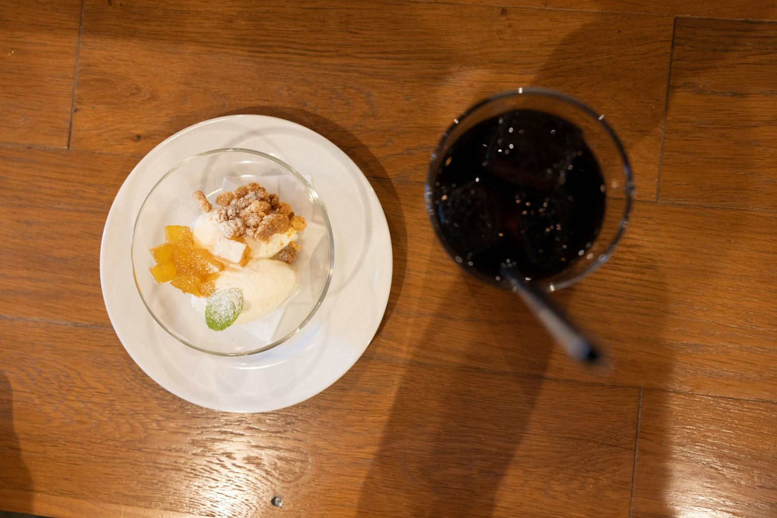 Puding dengan es krim dan buah di samping segelas cola di atas meja kayu