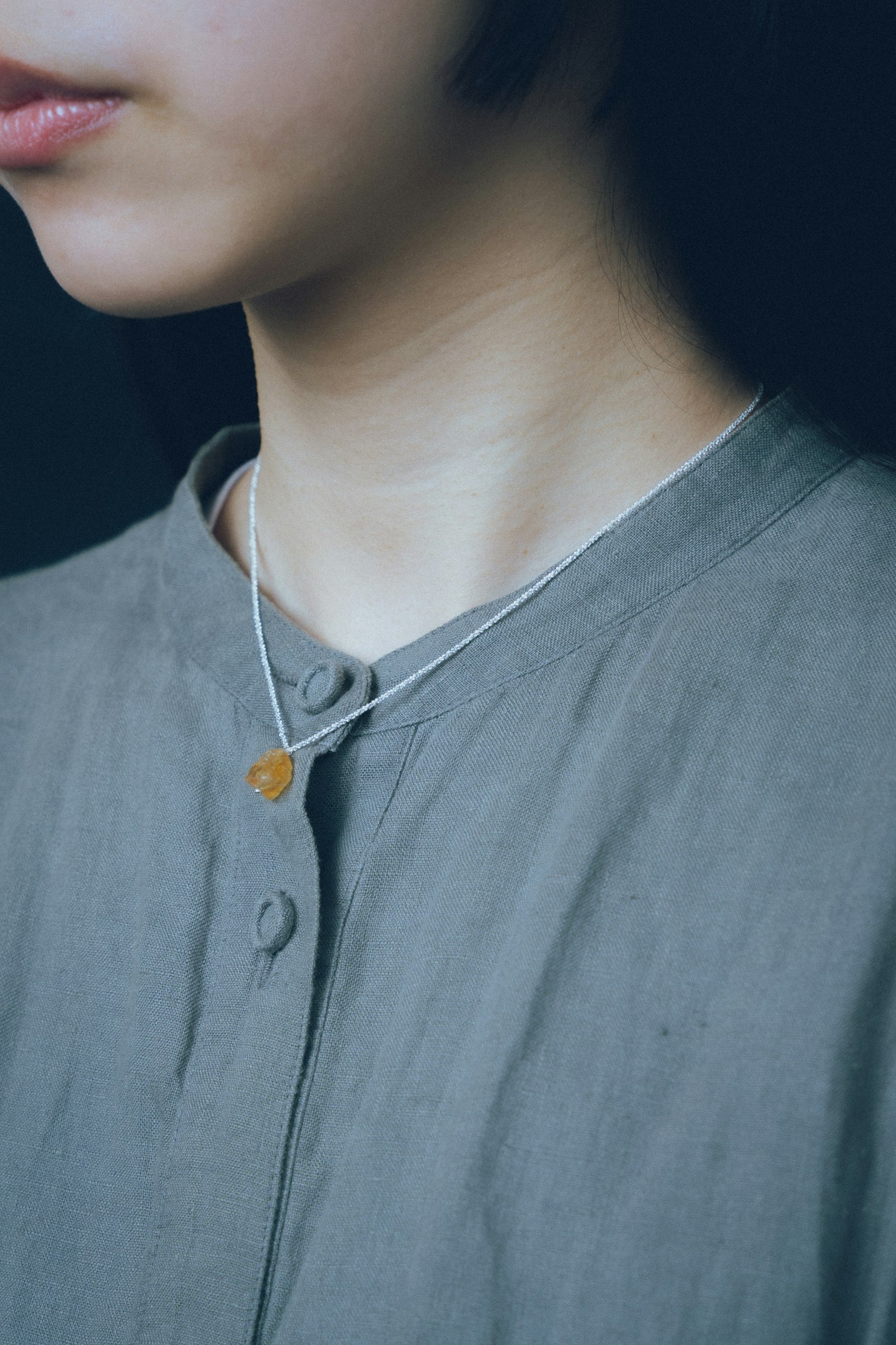Primer plano de una mujer con un collar simple y una blusa gris