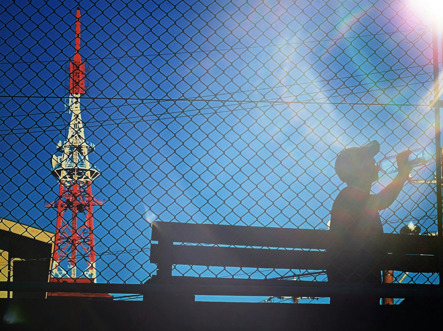 A child playing trumpet under a blue sky with a red and white communication tower