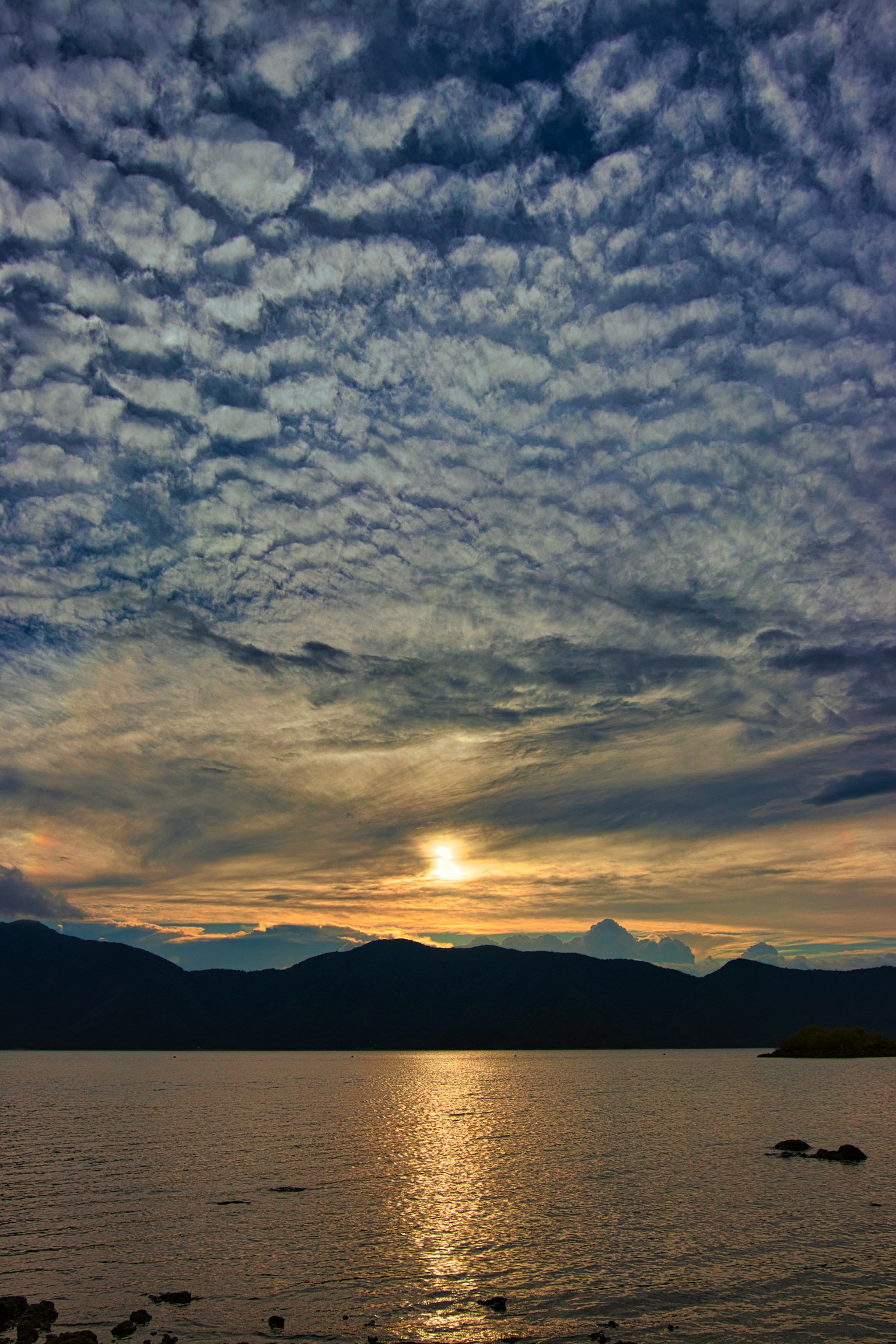 Tramonto sulle montagne con acqua riflettente e nuvole testurizzate