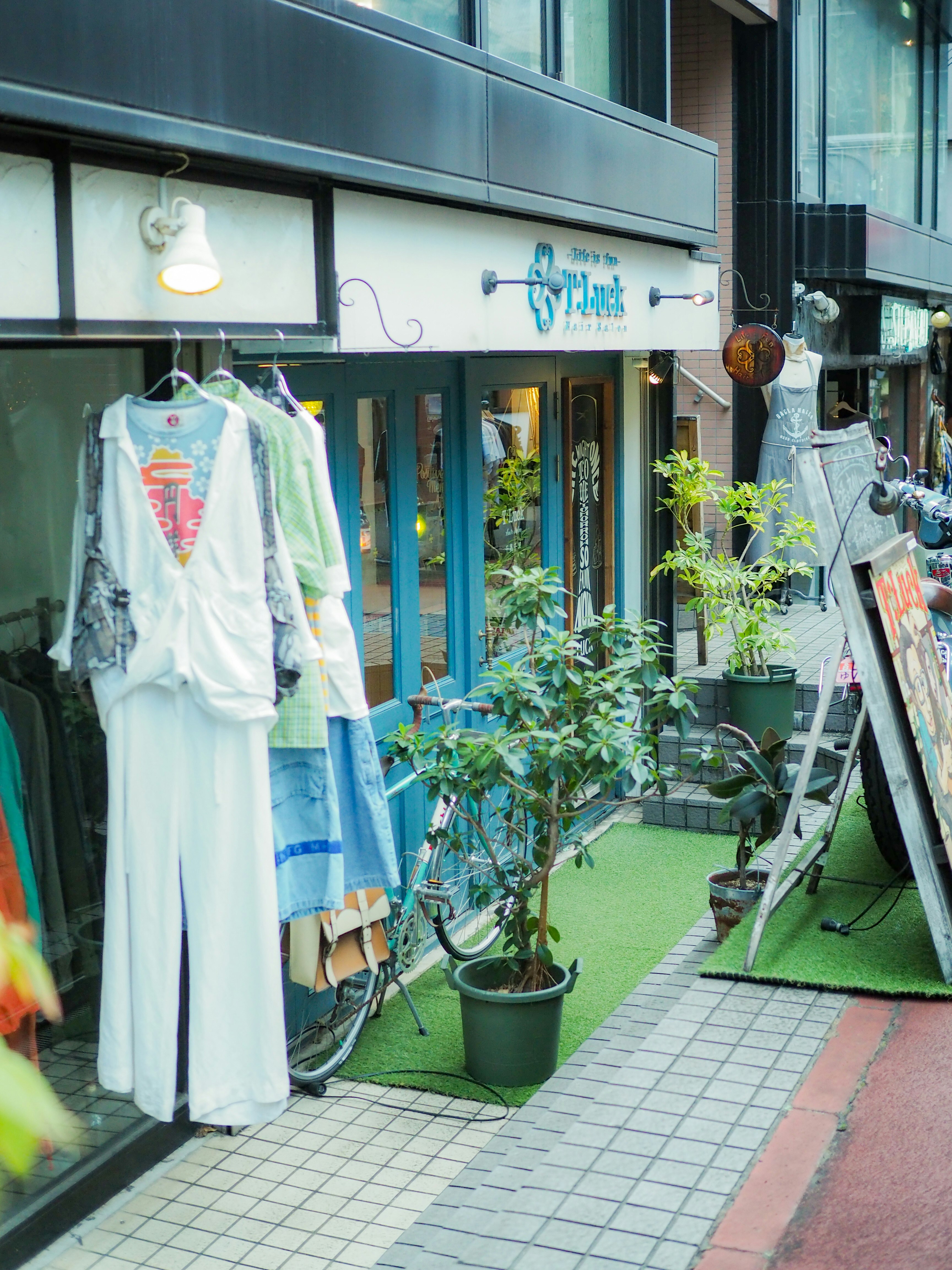 緑の芝生マットと衣類が並ぶ店先の小さな通路