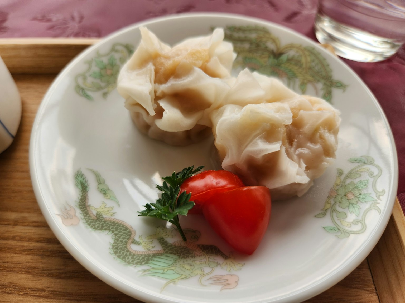 Plate featuring two shumai dumplings and a cherry tomato garnish