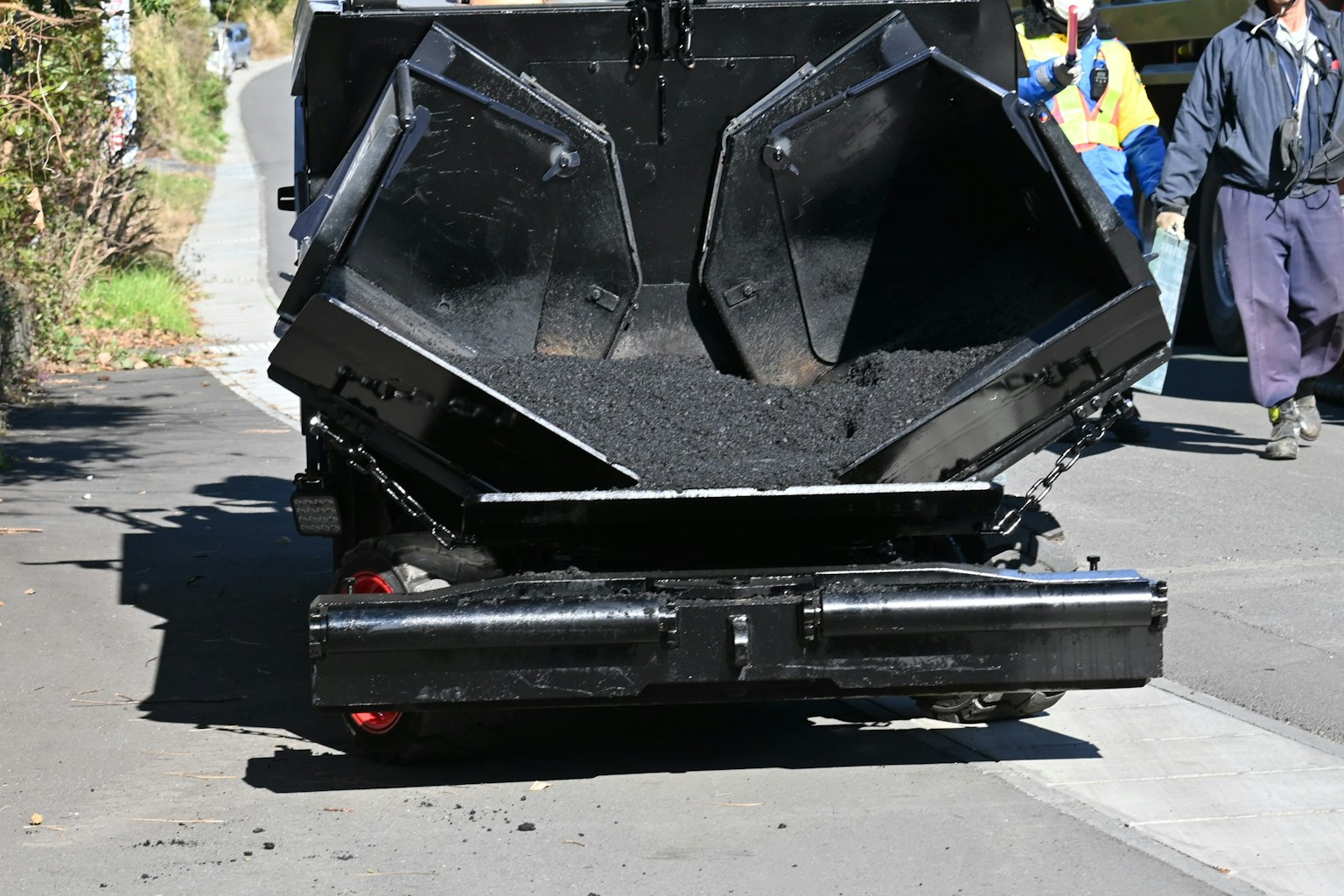 Rear view of a specialized asphalt paving vehicle with open hoppers