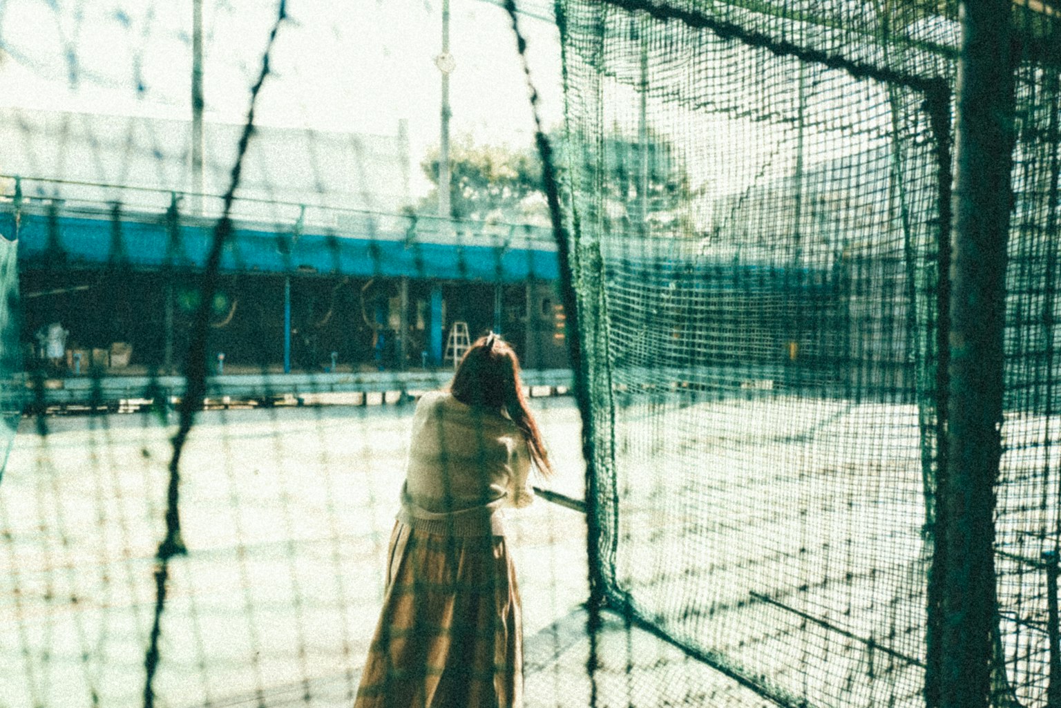 Mujer mirando hacia atrás a través de una red con una cancha de tenis al fondo