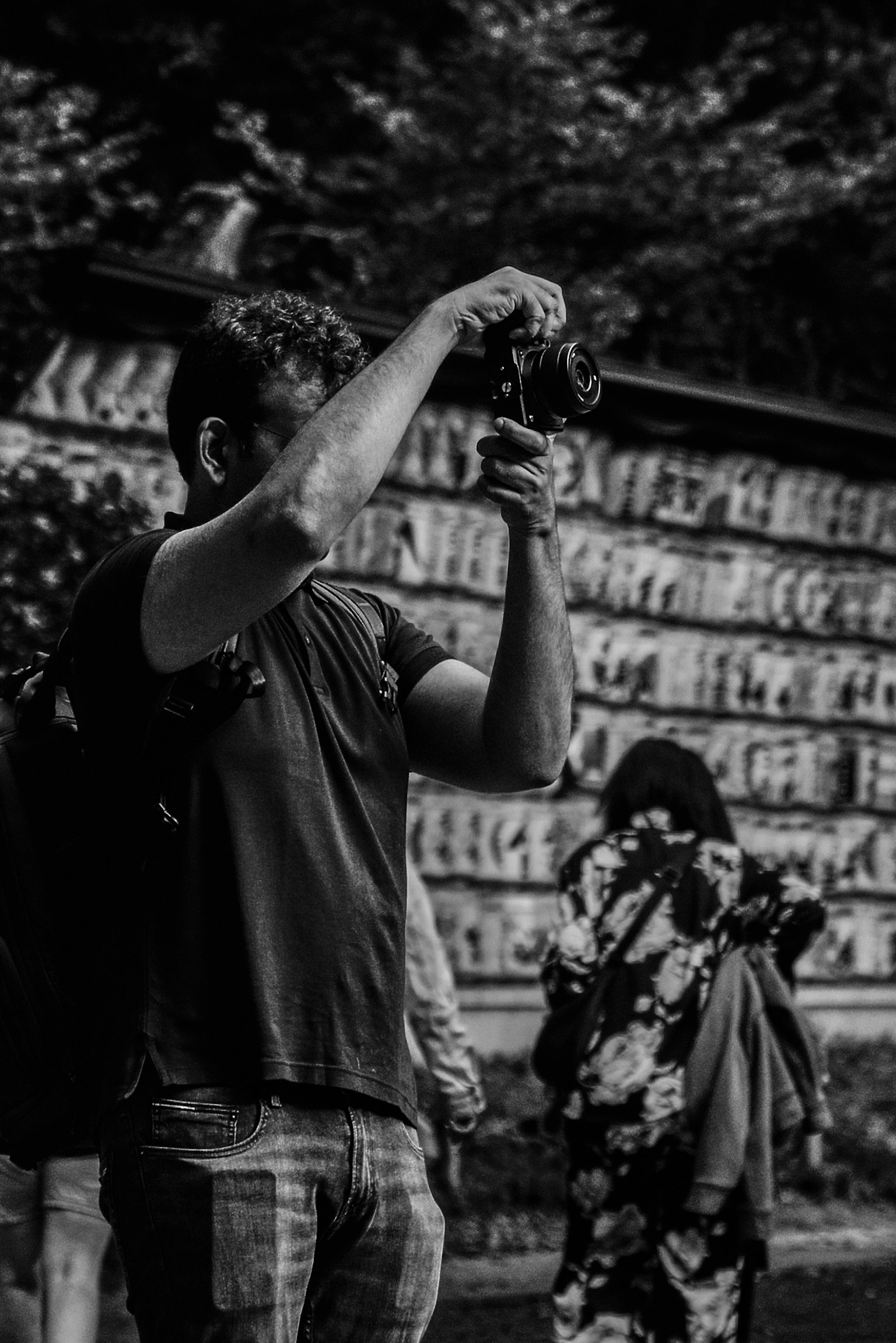 Foto en blanco y negro de un hombre sosteniendo una cámara con personas vestidas con ropa tradicional al fondo