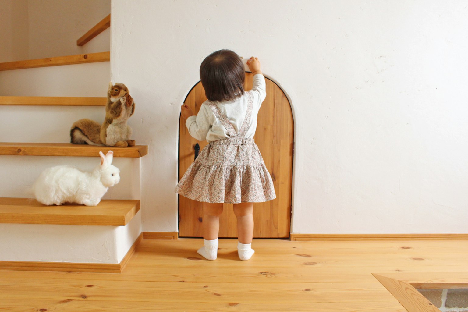 A young girl knocking on a wooden door with a rabbit and a dog nearby by the stairs