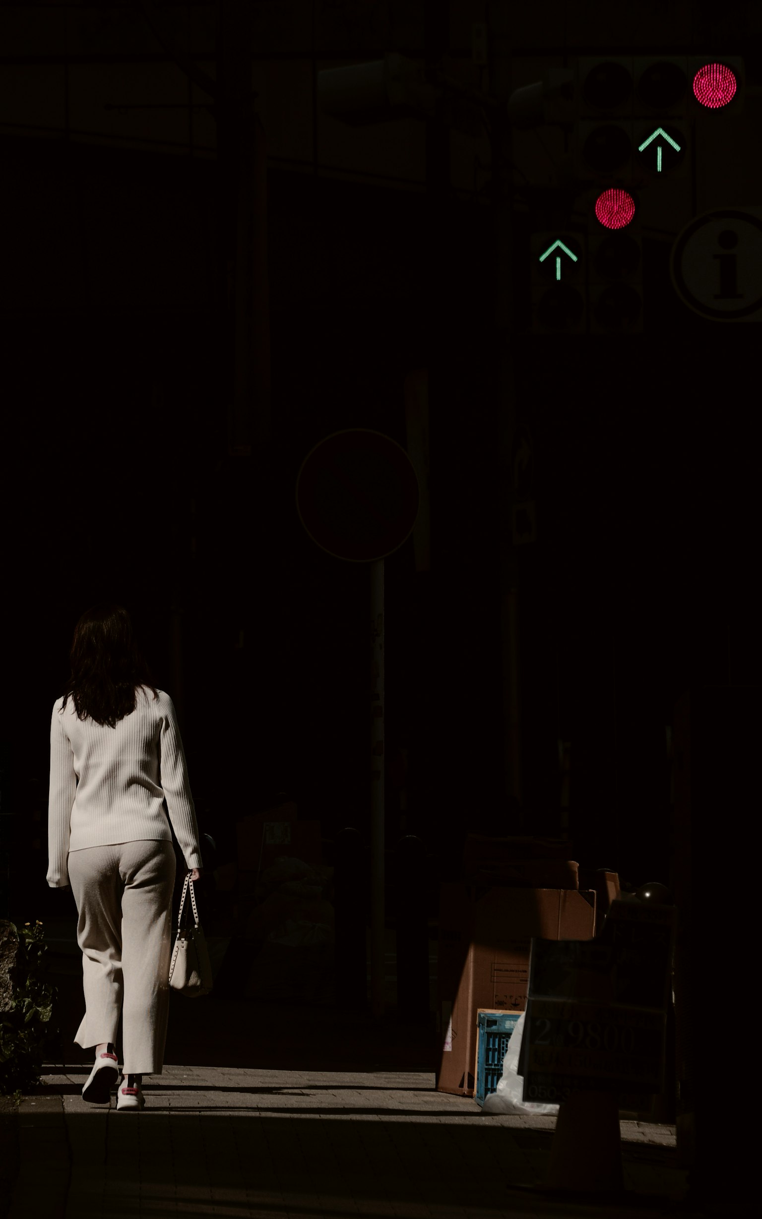 Mujer con atuendo blanco caminando en una calle oscura semáforos al fondo