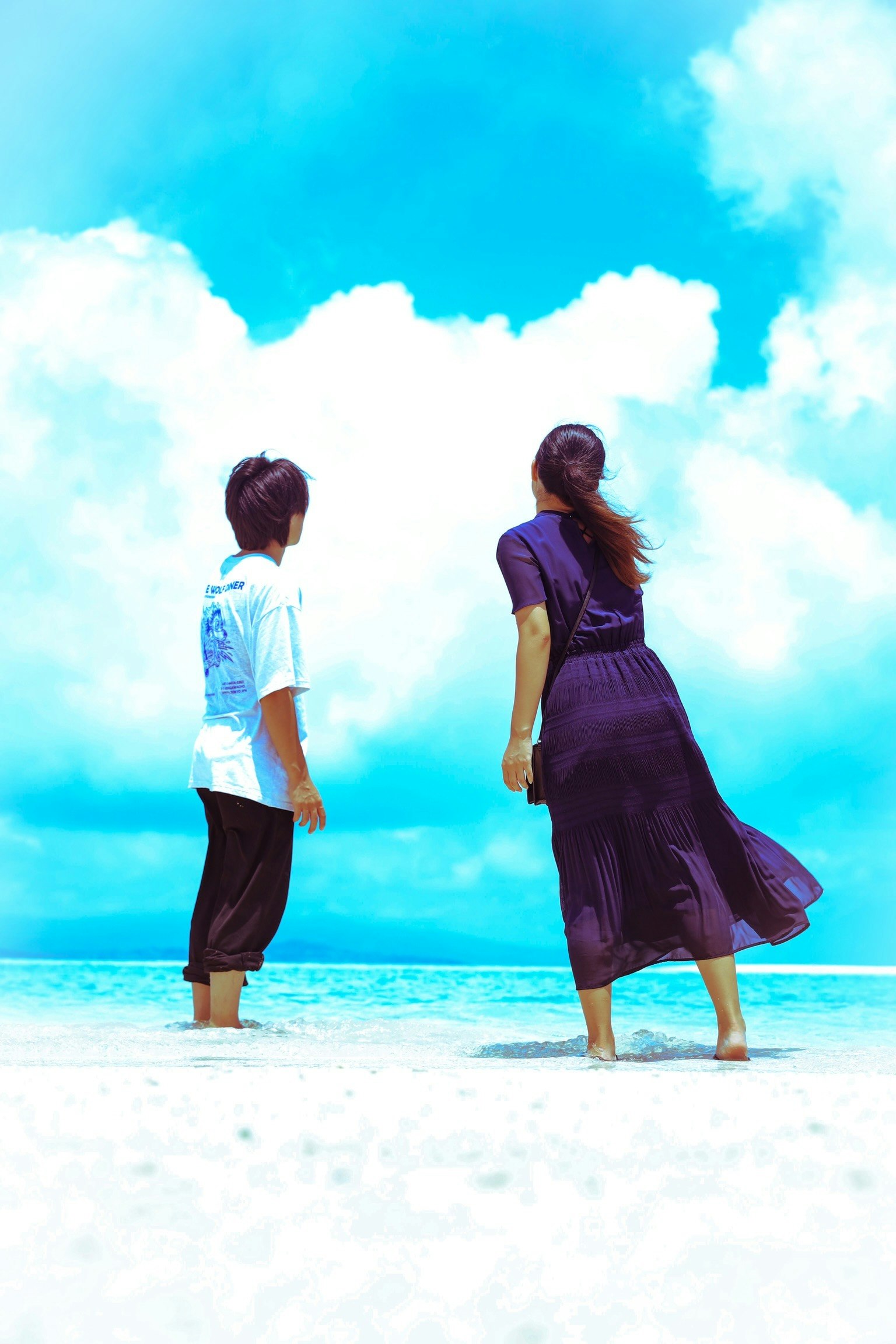 Vista posterior de un hombre y una mujer de pie en la playa con un cielo y mar azul brillante