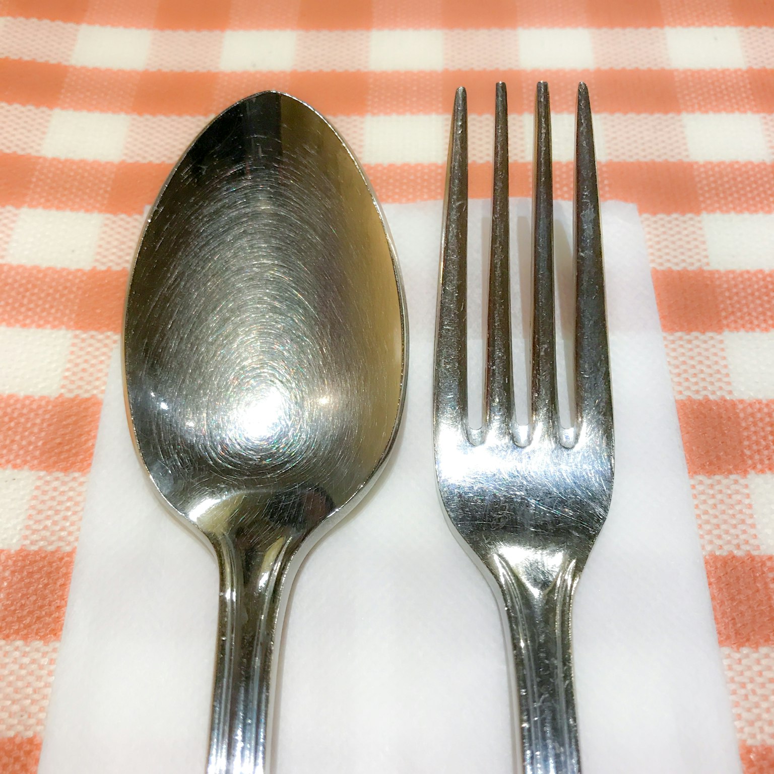 Una cuchara y un tenedor colocados sobre una servilleta blanca en un mantel a cuadros