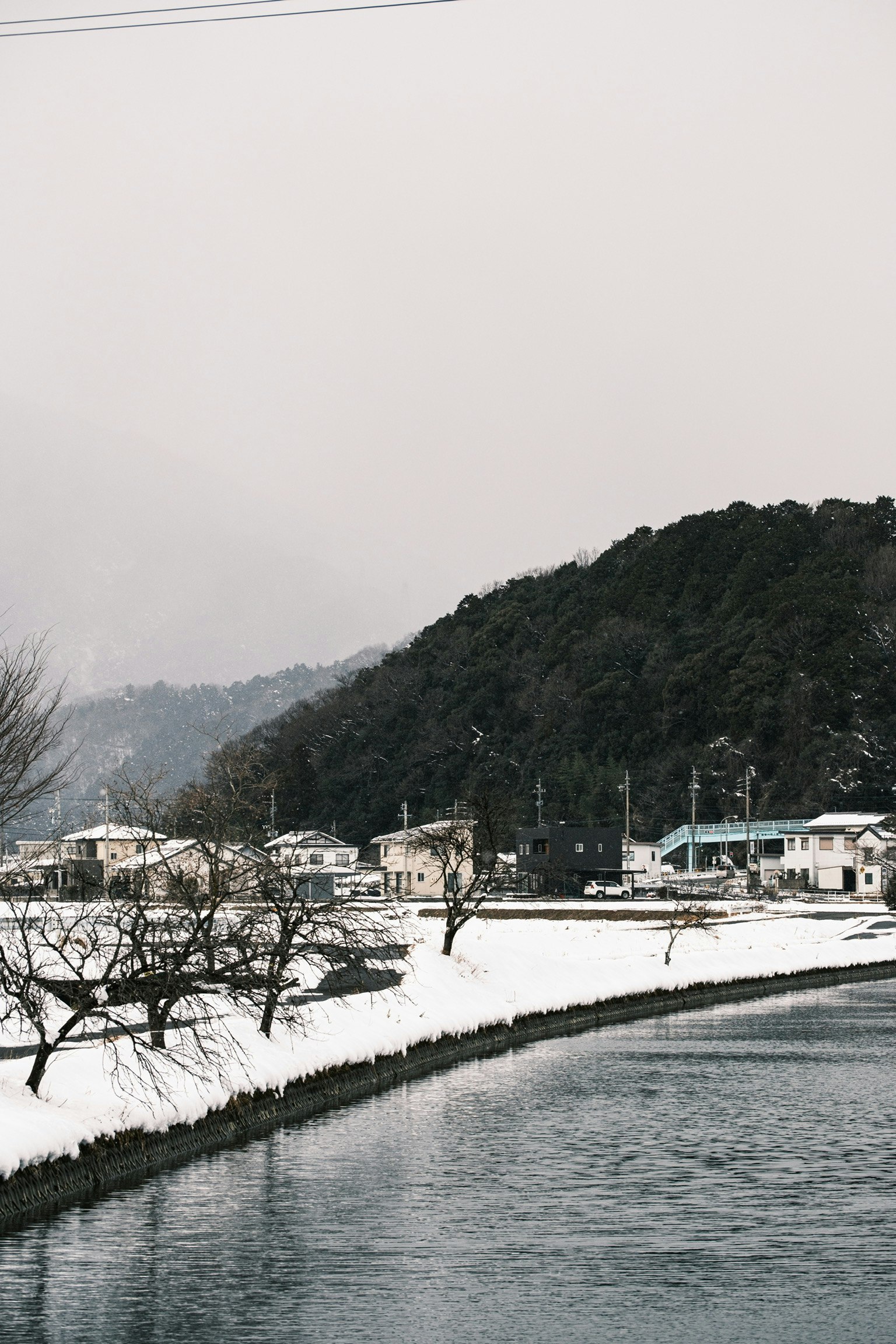 被雪覆盖的村庄沿河而建，背景是山脉
