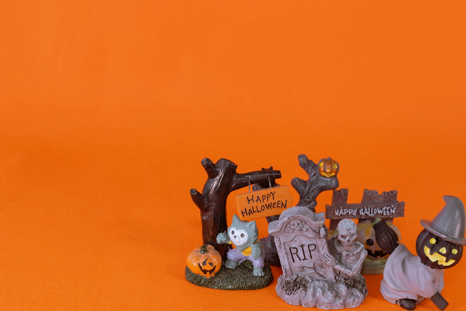 Halloween-Dekorationen mit einem Geist, Grabsteinen, Kürbissen und einer Hexe vor orangefarbenem Hintergrund