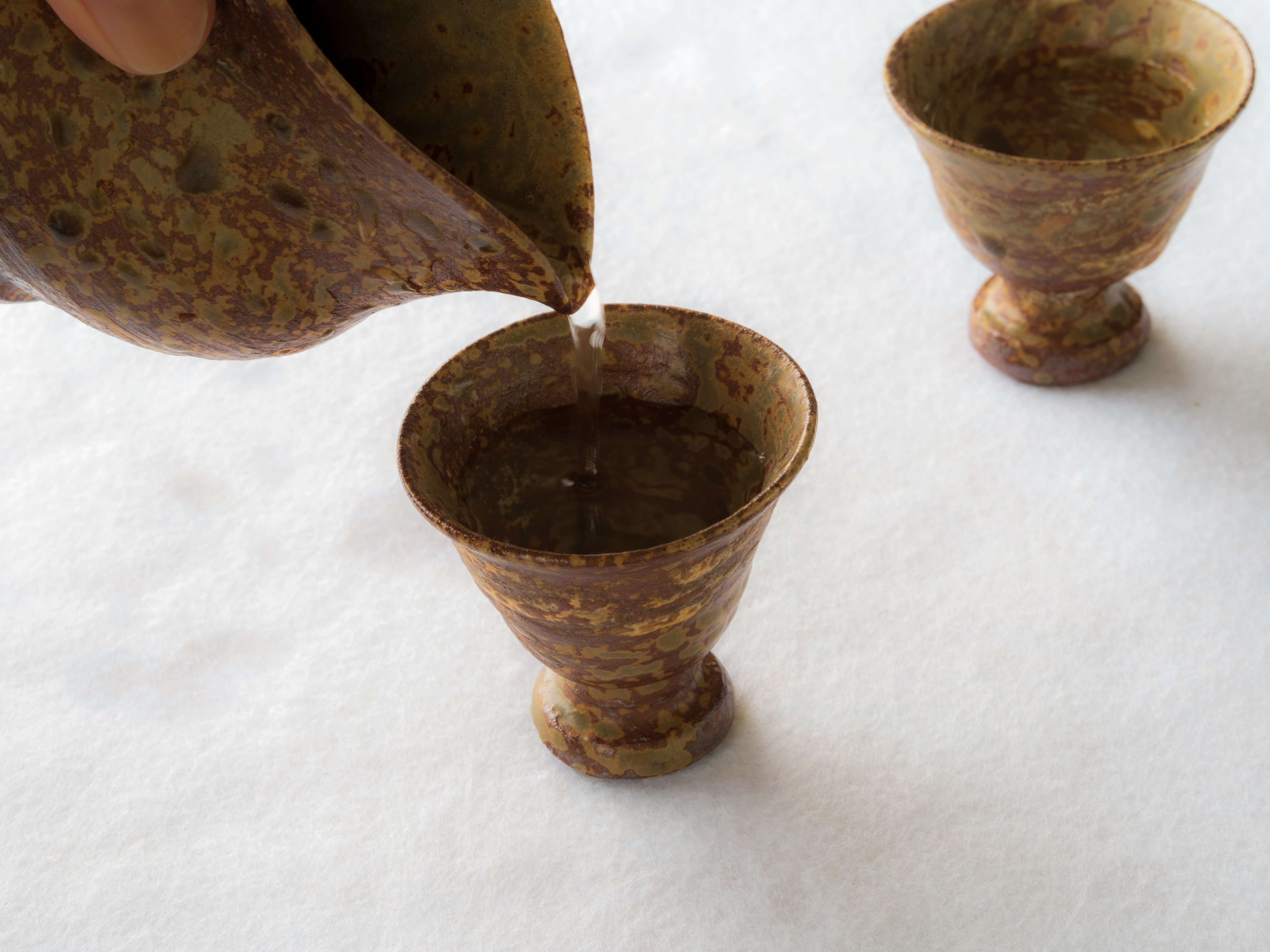 Brown ceramic cups with liquid being poured