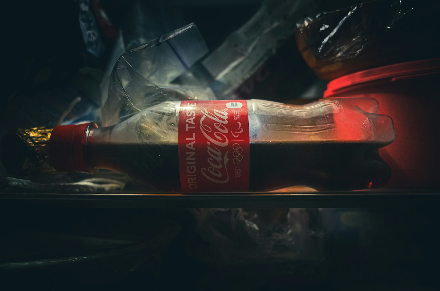 Chai Coca-Cola đặt trong tủ lạnh xung quanh là bao bì nhựa