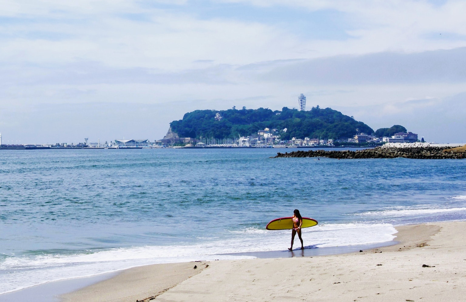 海滩上一个孩子手持冲浪板，远处有一个岛屿