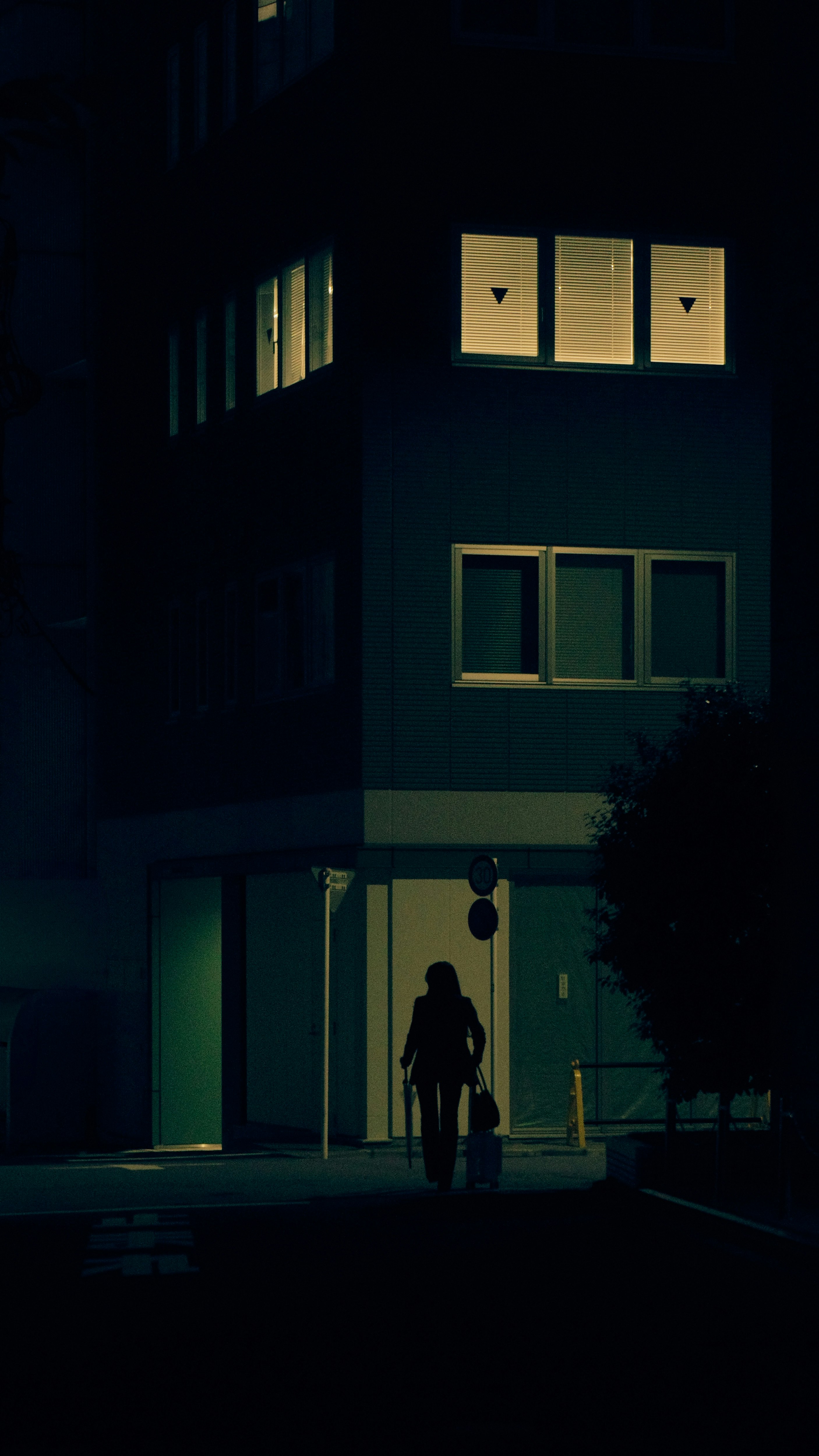 雨上がりの夜、傘をさすシルエットの人物が並ぶ街並み