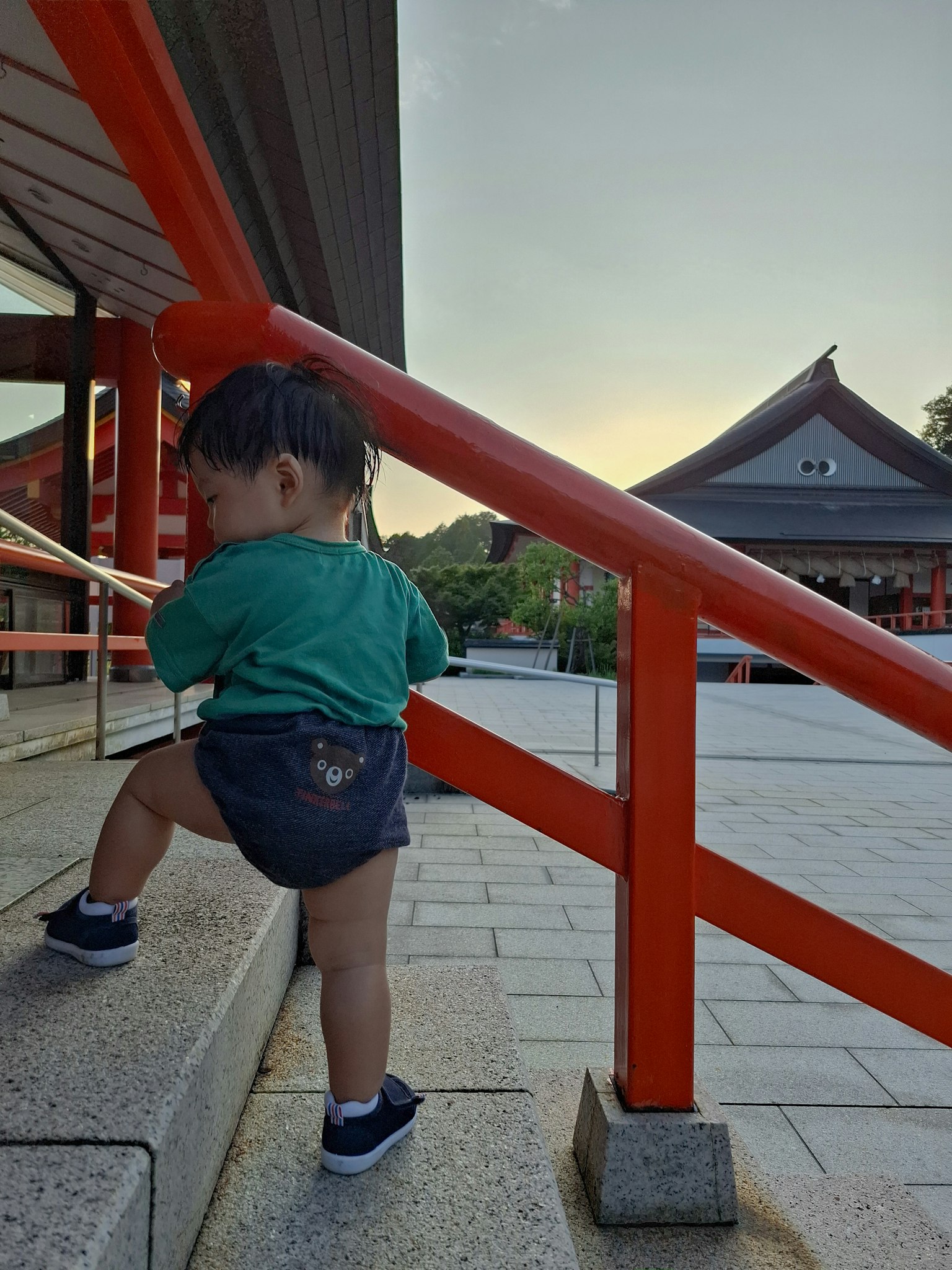 孩子在日落时分于神社的红色扶手旁爬楼梯